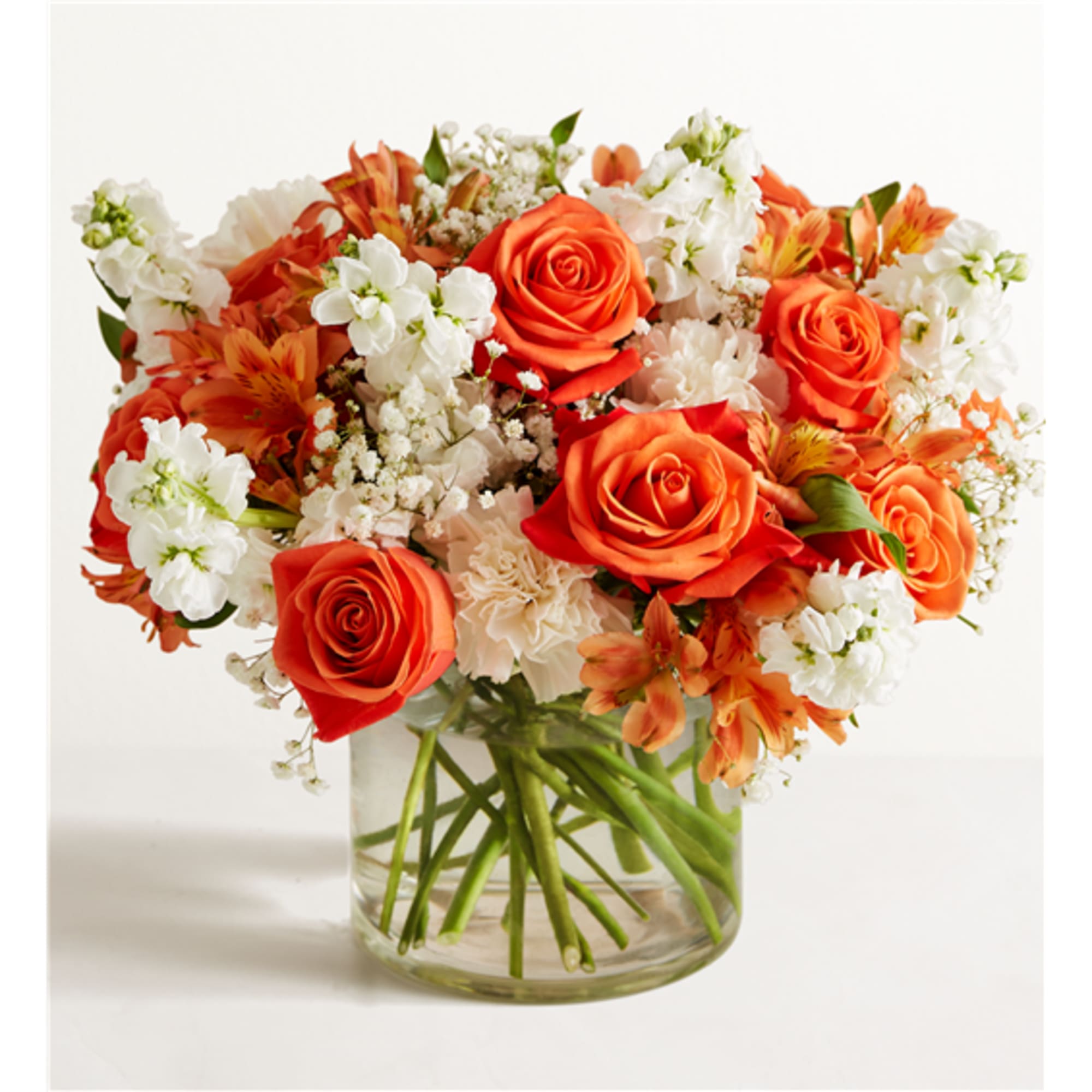 Orange roses and white flowers arranged in a clear glass vase