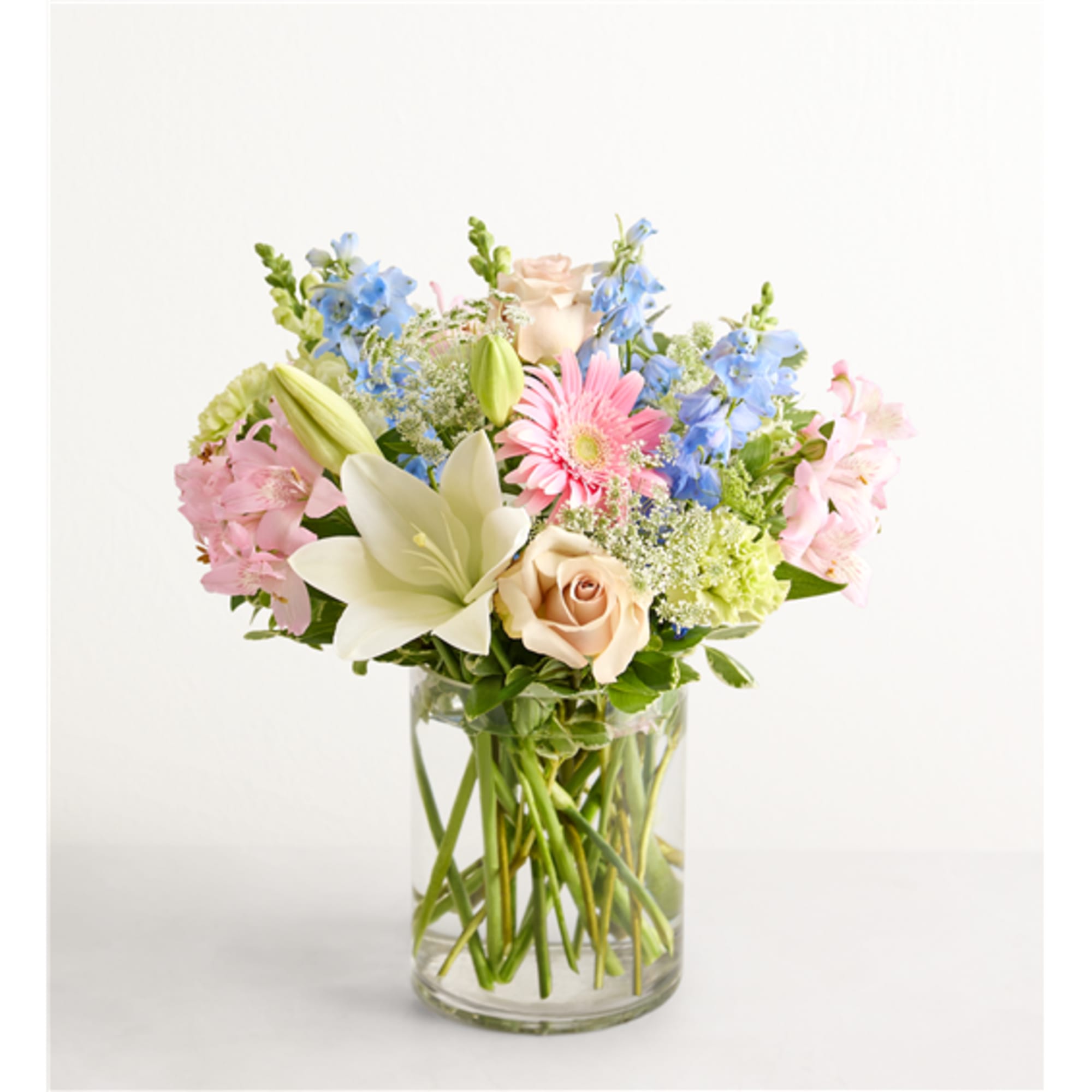 Mixed pastel bouquet in a clear glass vase with lilies, roses, and daisies