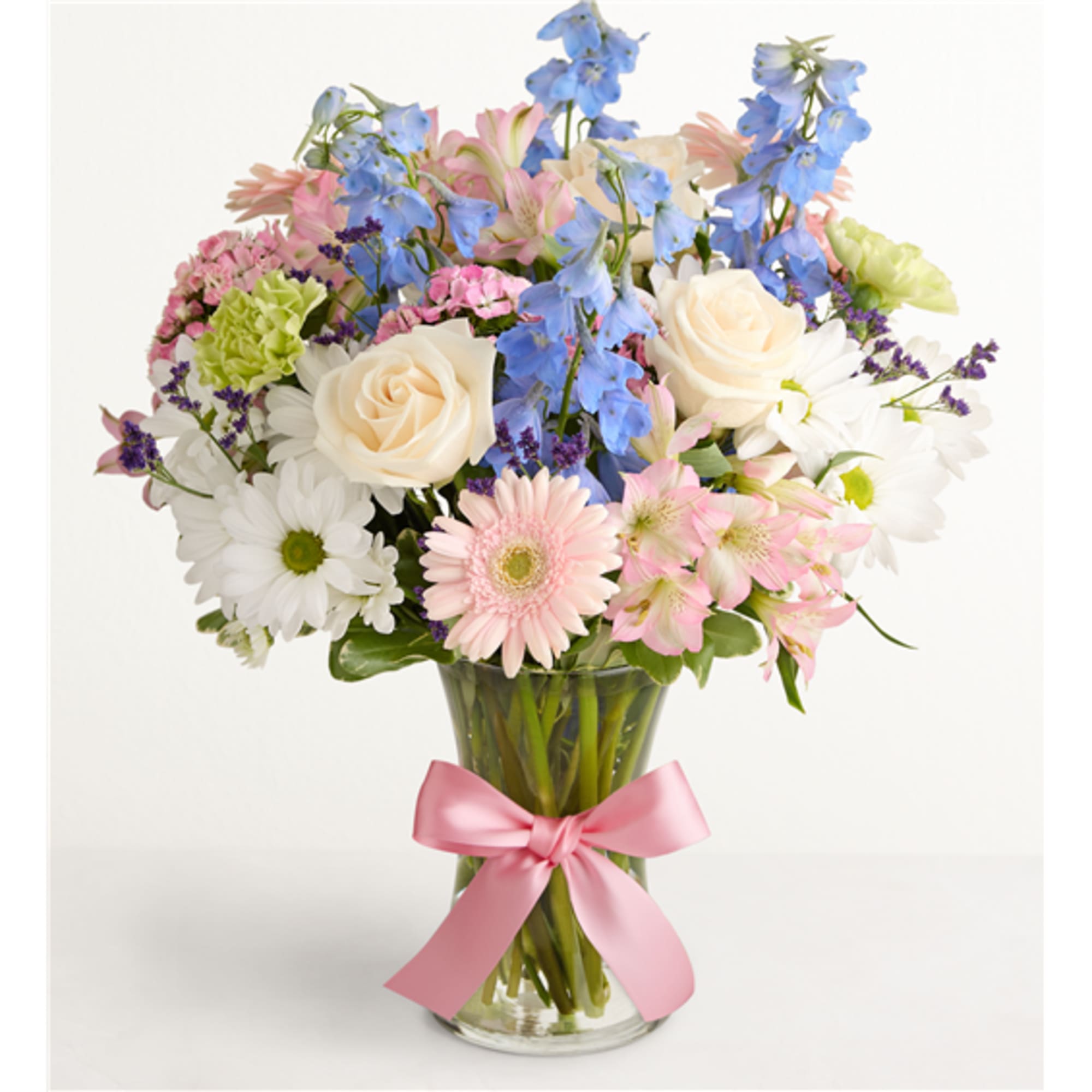 Mixed bouquet of pastel flowers in a clear glass vase with a pink ribbon