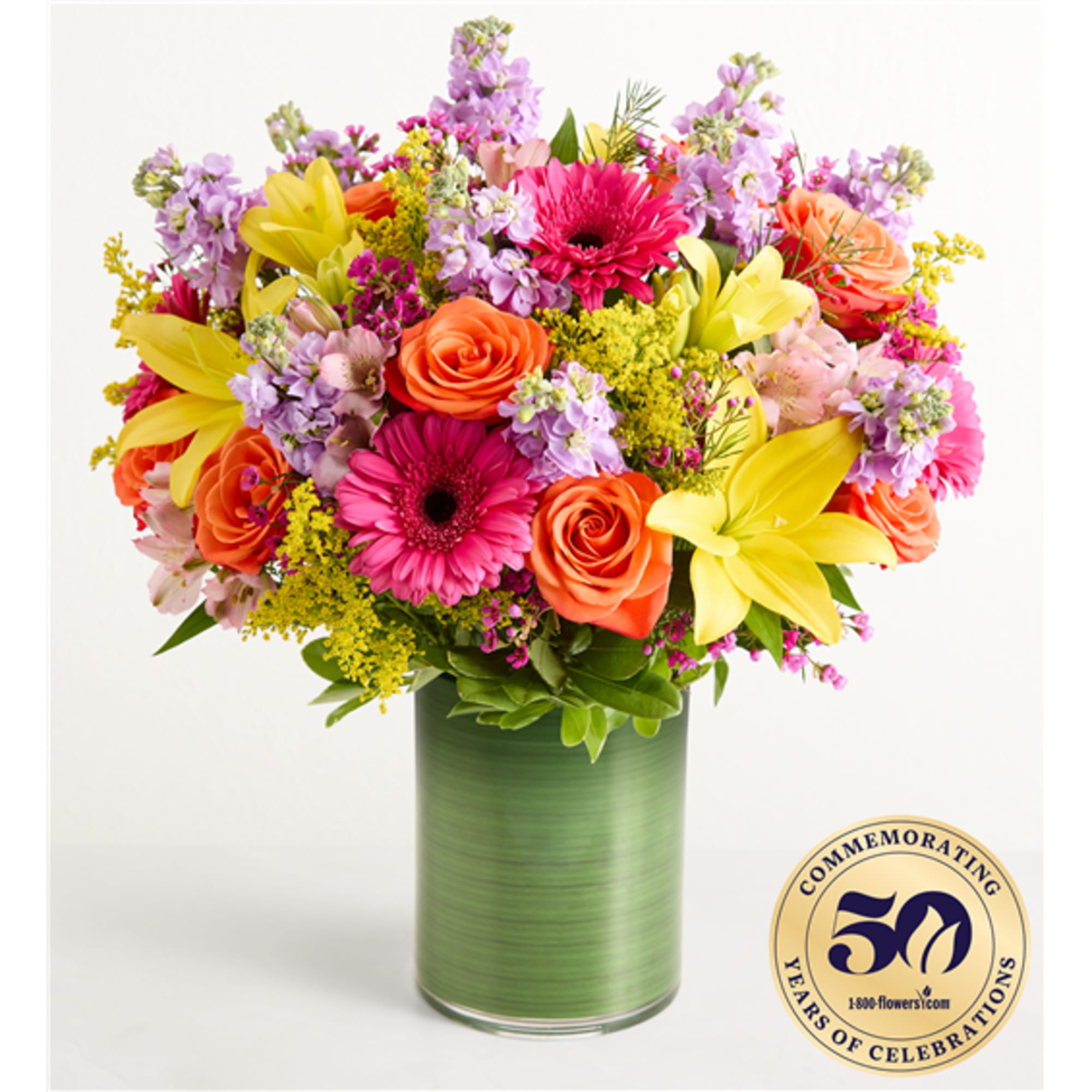 Bright mixed bouquet with roses, gerbera daisies, lilies, and purple blooms in a green vase