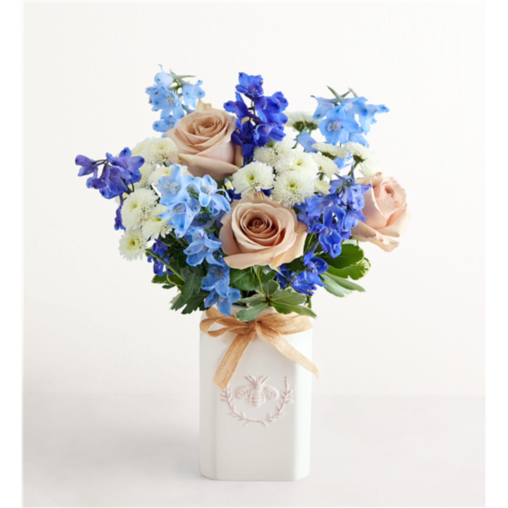 Bouquet of peach roses, blue flowers, and white blooms in a white vase