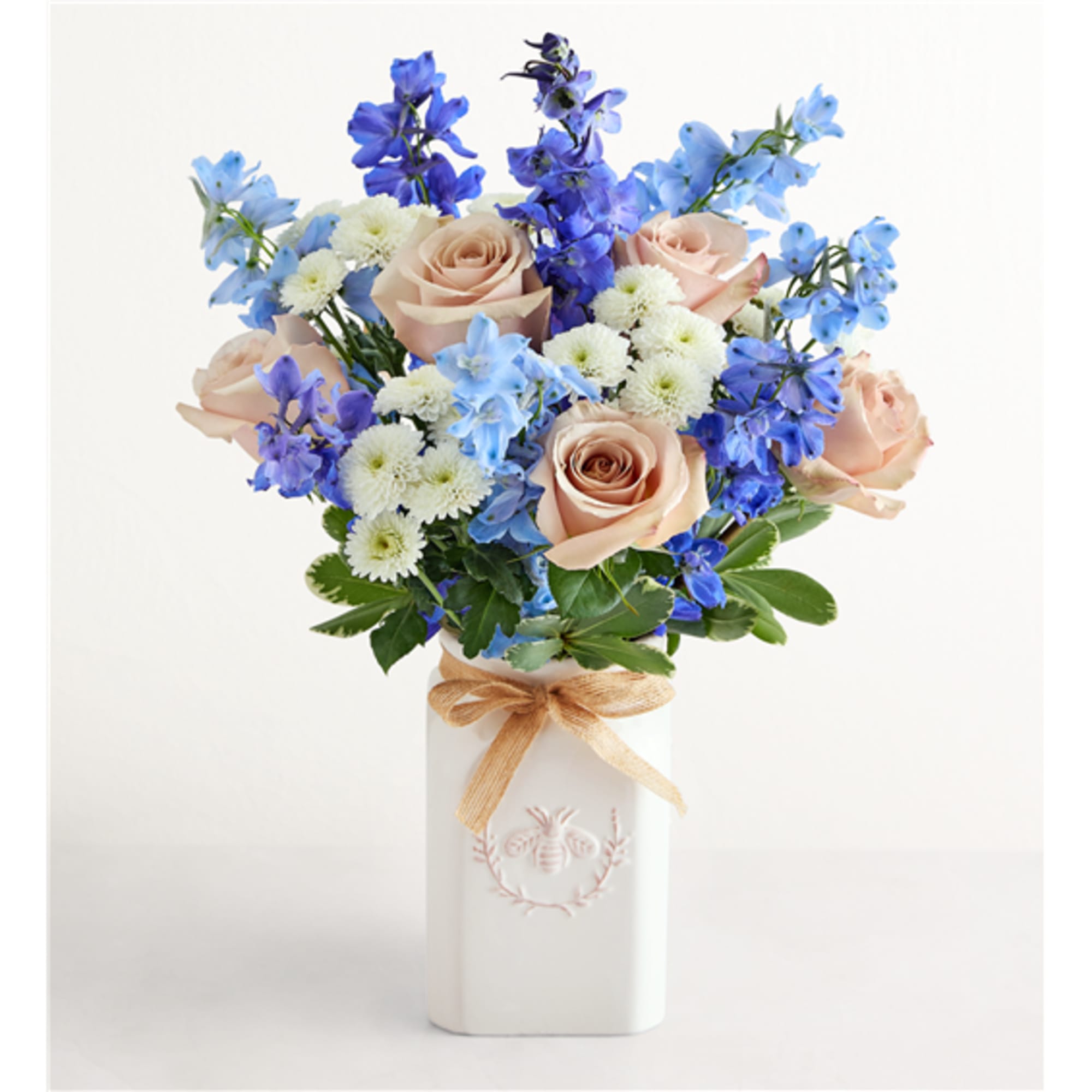 Bouquet of peach roses, blue flowers, and white daisies in a white vase
