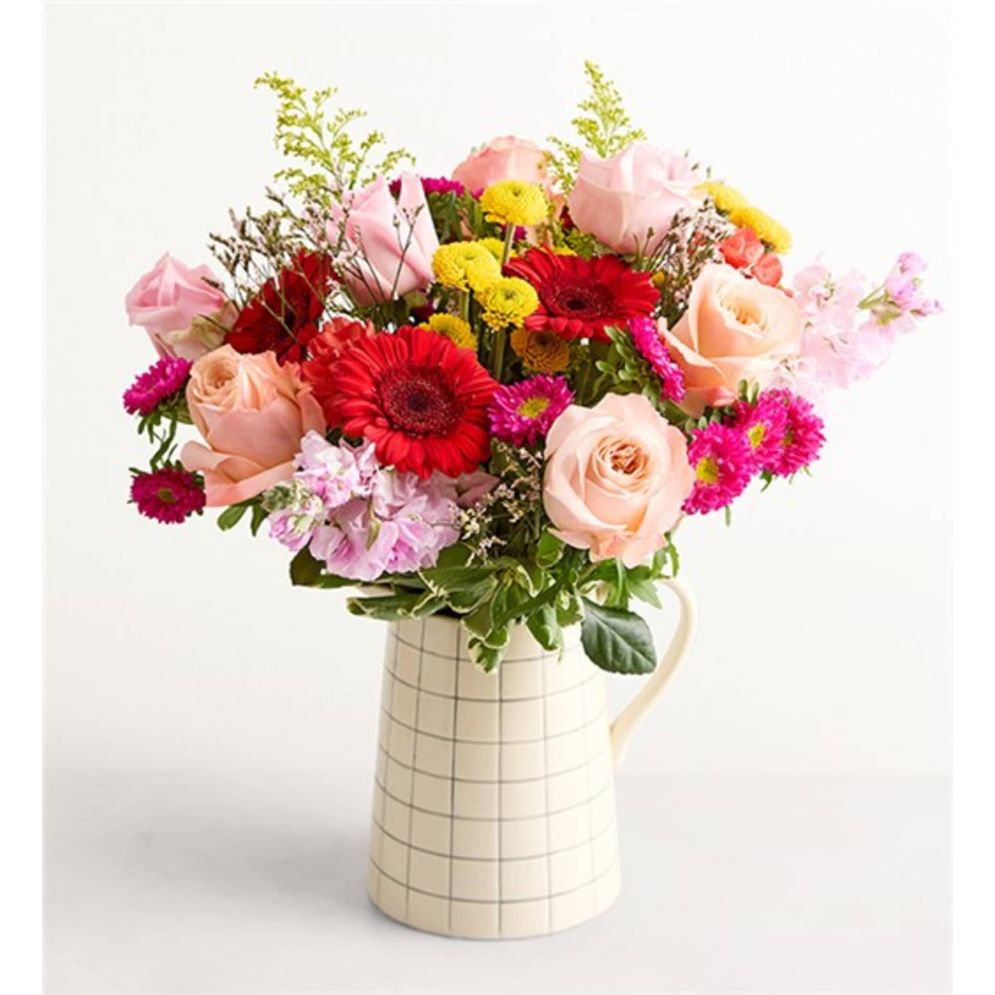 Mixed pink and red flowers arranged in a checkered ceramic pitcher