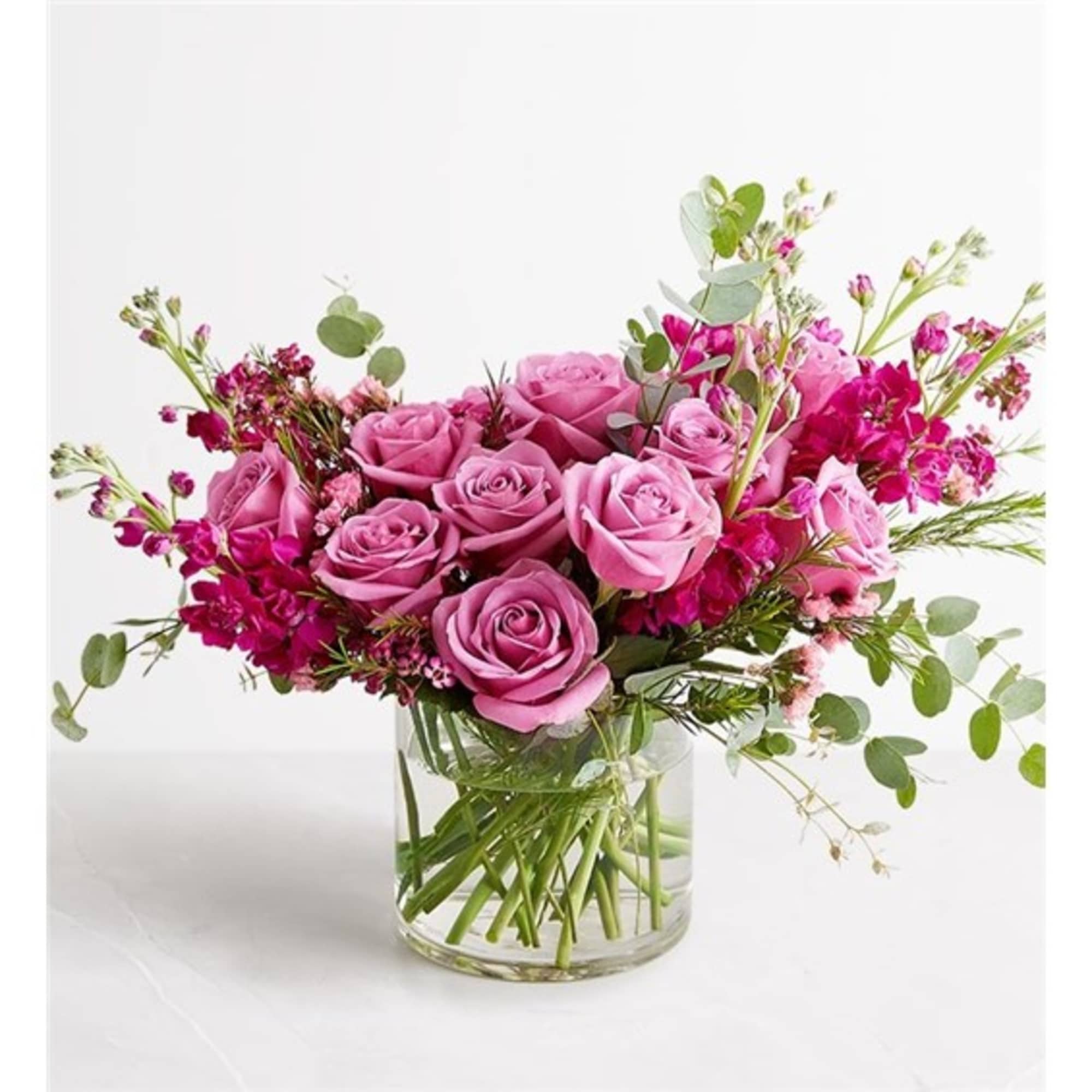 Pink roses and magenta flowers arranged in a clear glass vase