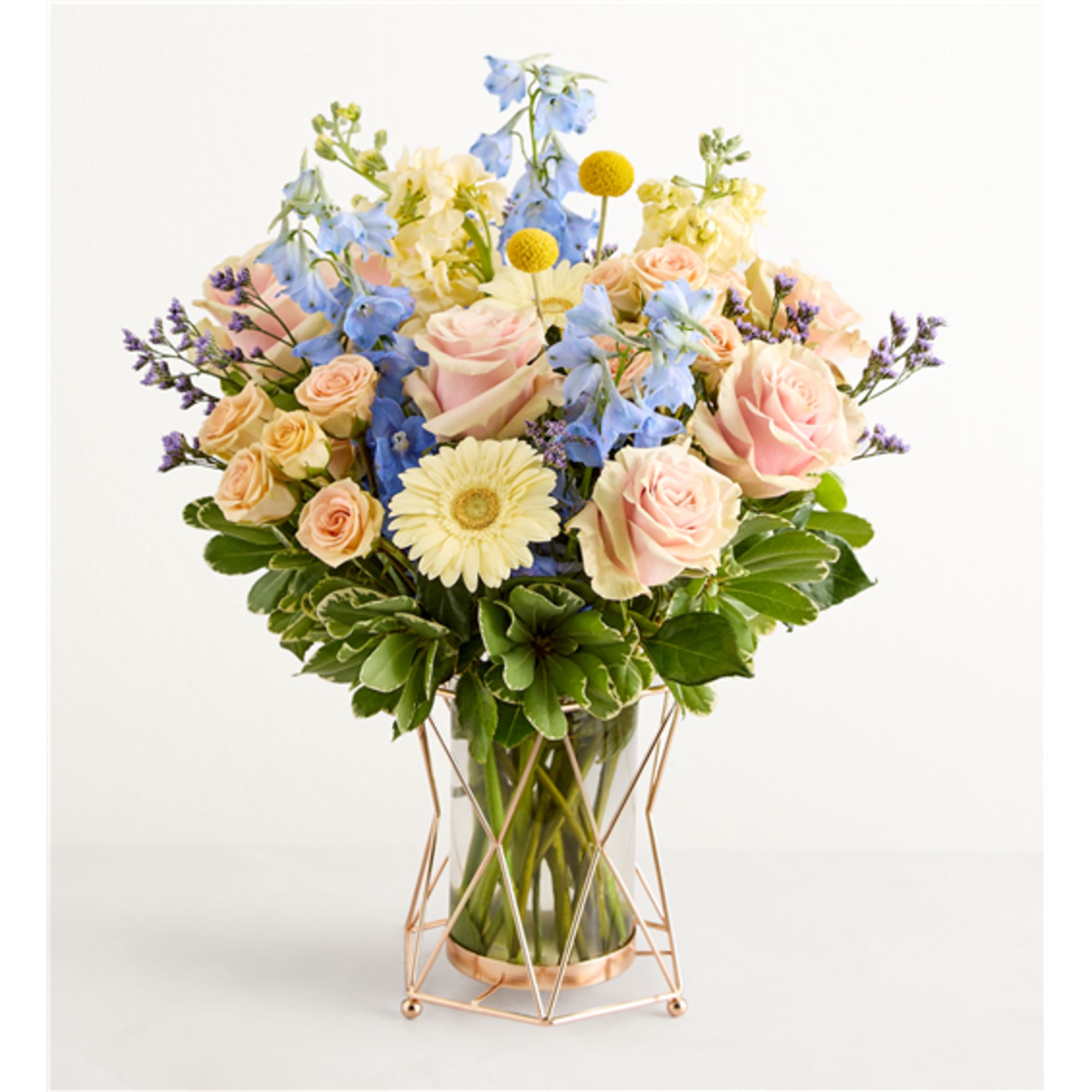 Pastel bouquet of roses, blue flowers, and a white daisy in a glass vase