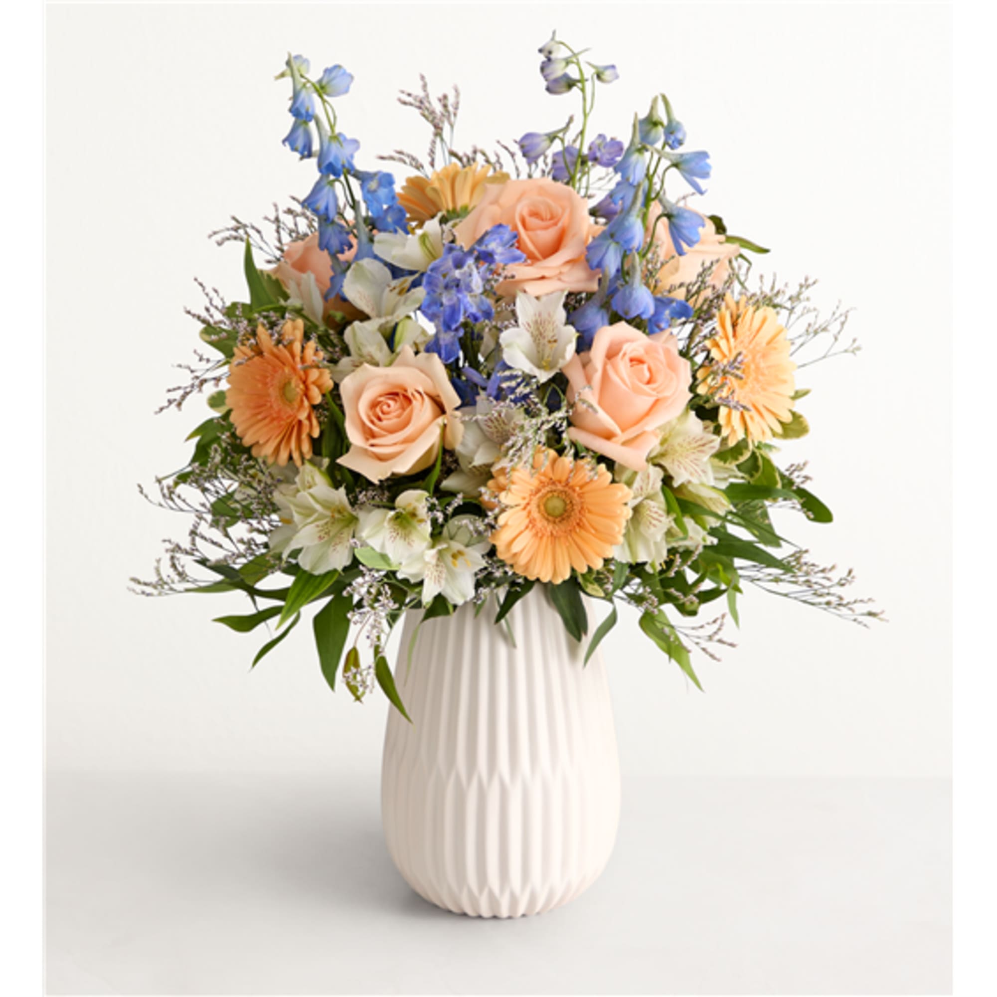 Peach roses and blue flowers arranged in a white vase