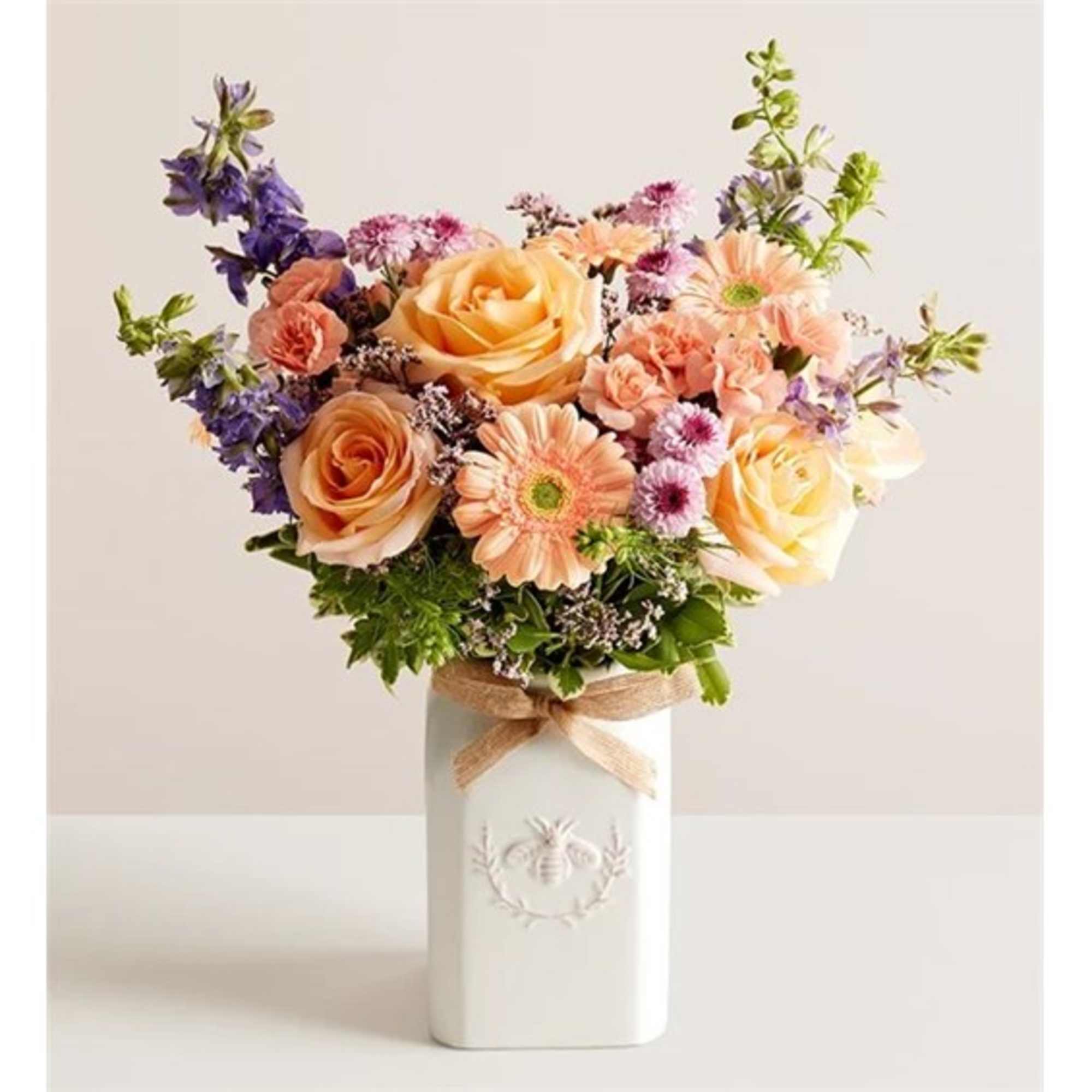 Mixed bouquet of peach roses and pastel daisies in a white vase