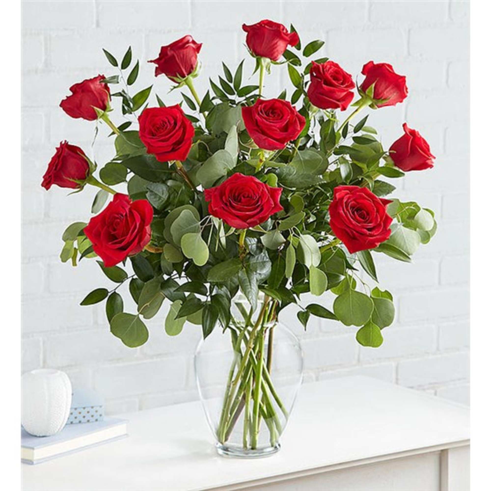 Red roses arranged in a clear glass vase with greenery