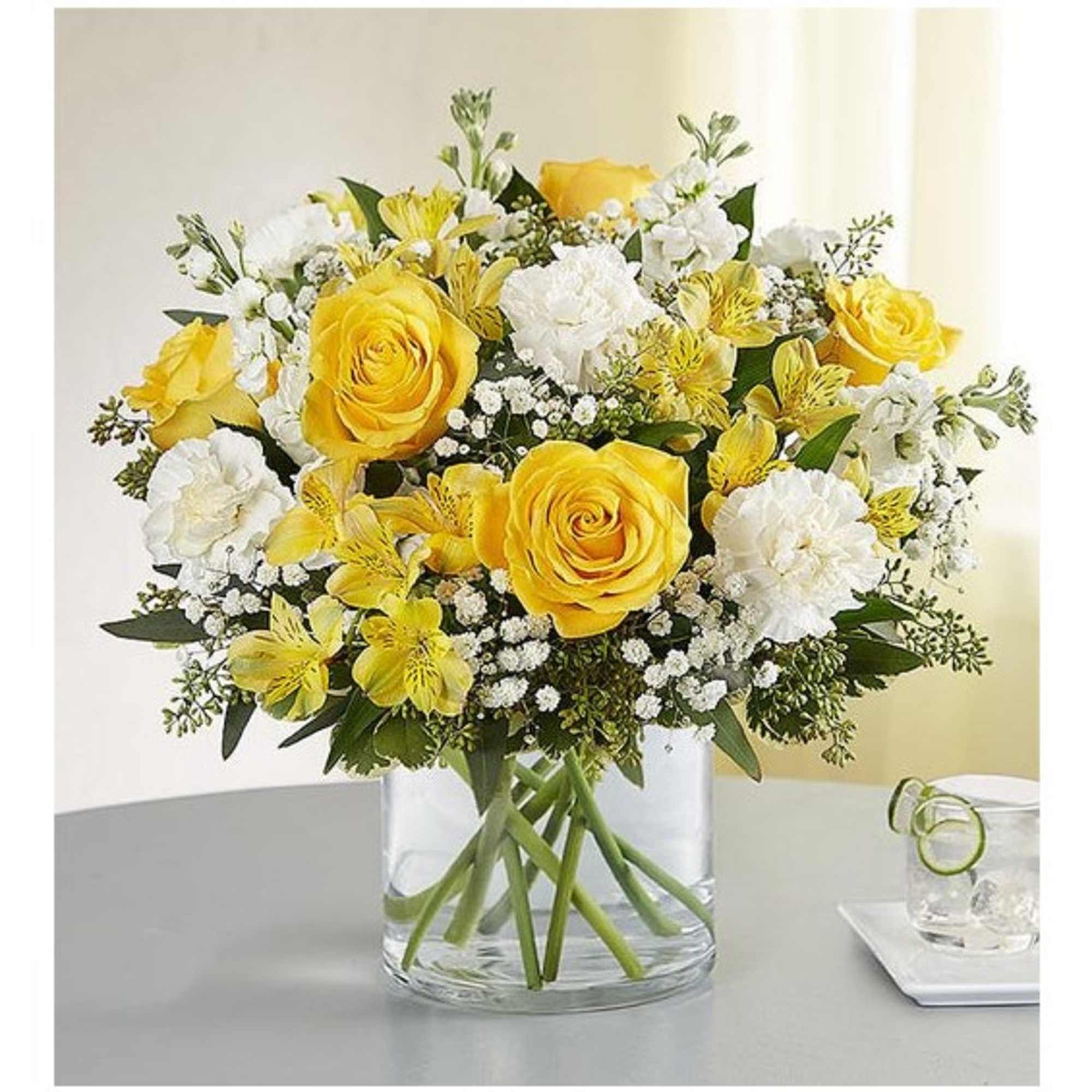 Yellow roses and white flowers arranged in a clear glass vase