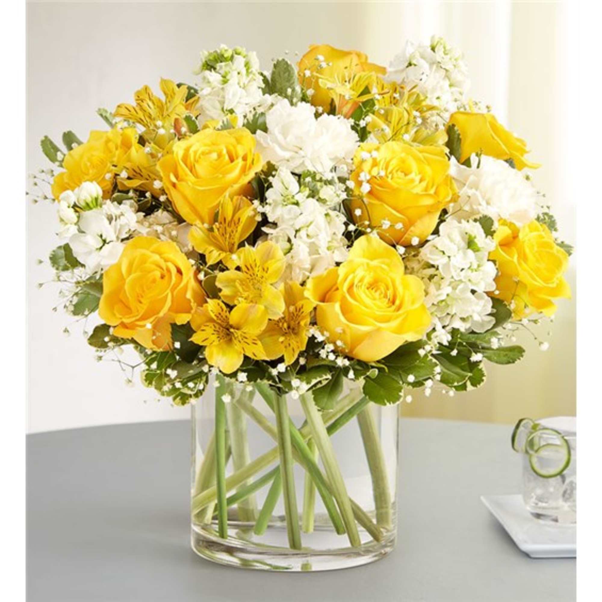 Yellow roses and white flowers arranged in a clear glass vase