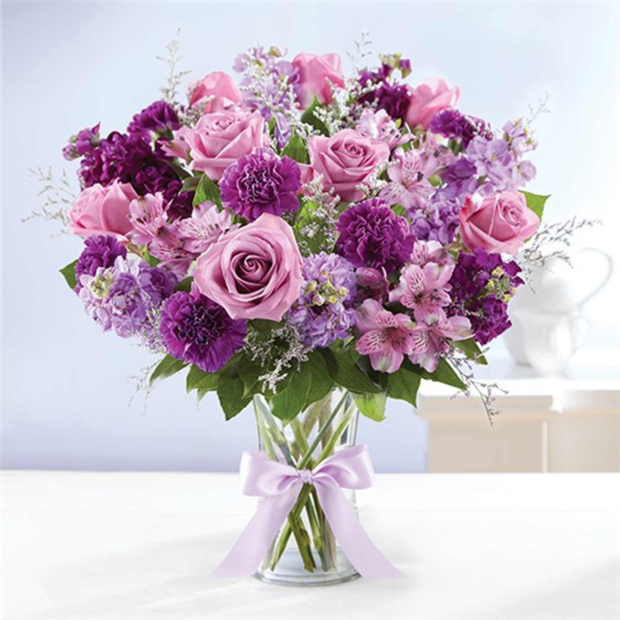 Pink and purple bouquet of roses and mixed flowers in a glass vase with a ribbon