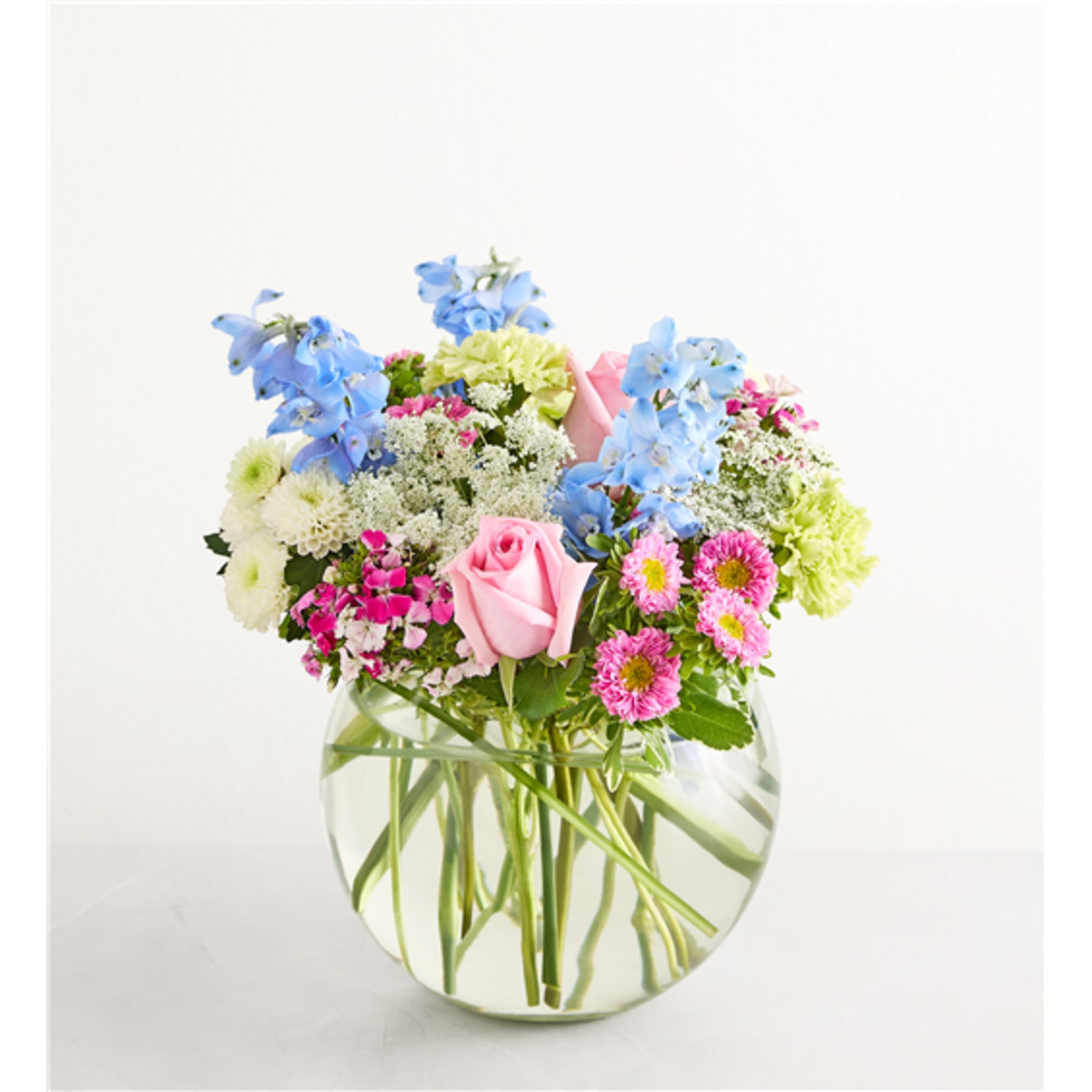 Mixed bouquet of pink, blue, and white flowers in a clear glass vase