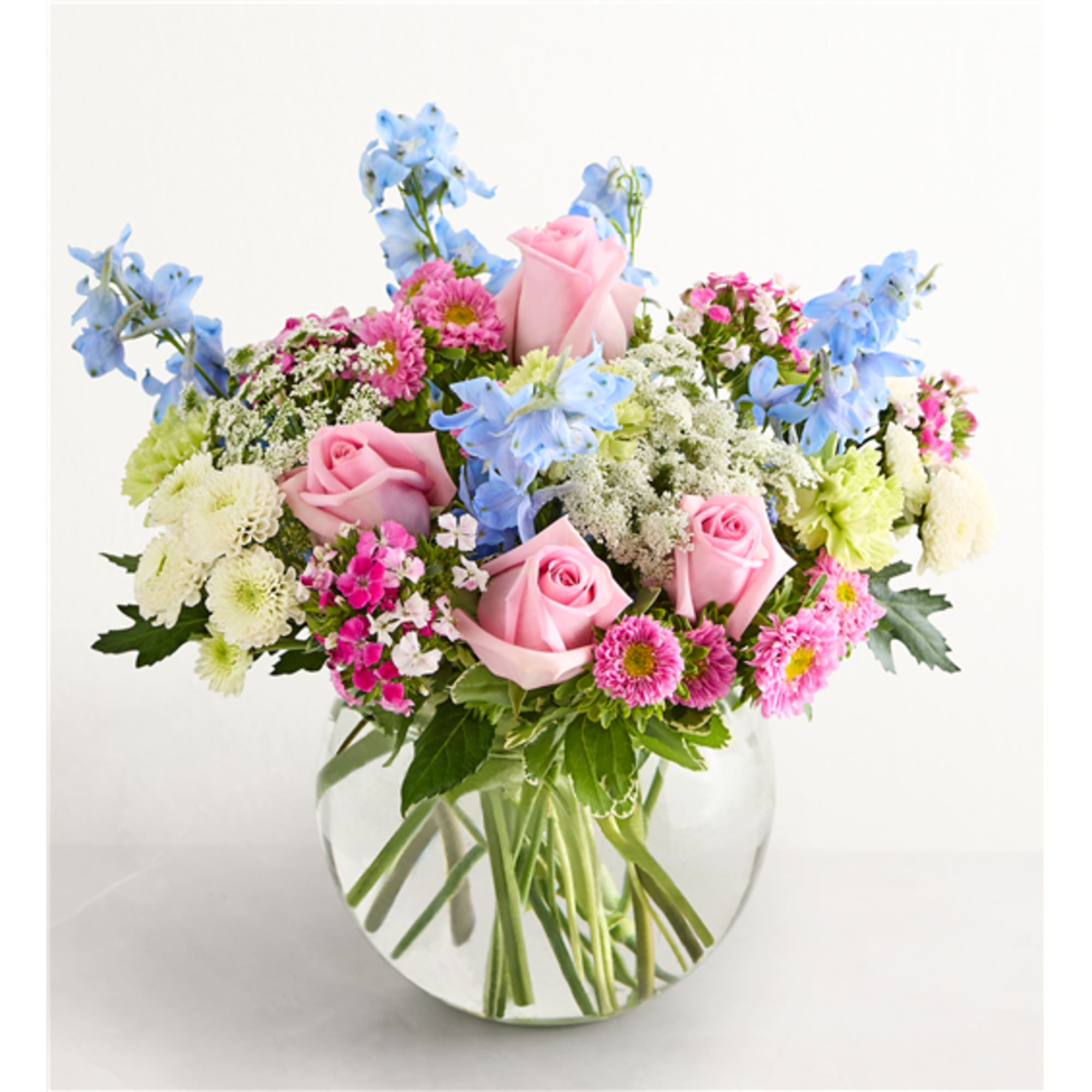 Mixed bouquet of pink roses, blue flowers, and white blooms in a glass vase