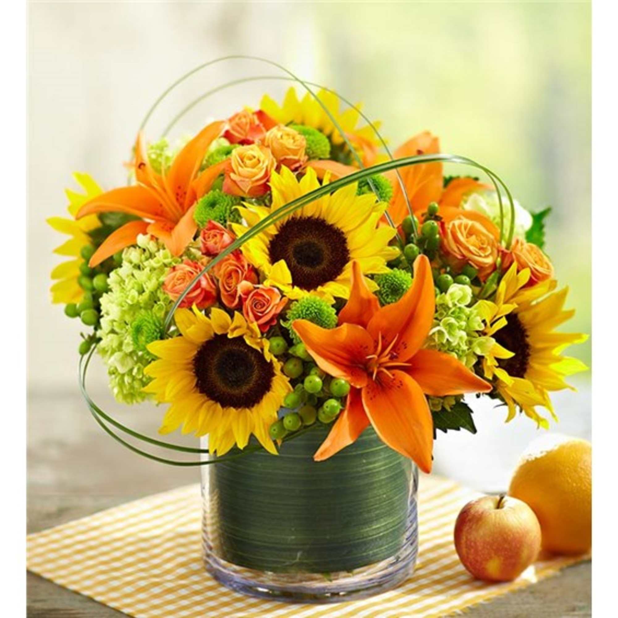 Bright bouquet of sunflowers, orange lilies, and roses in a glass vase
