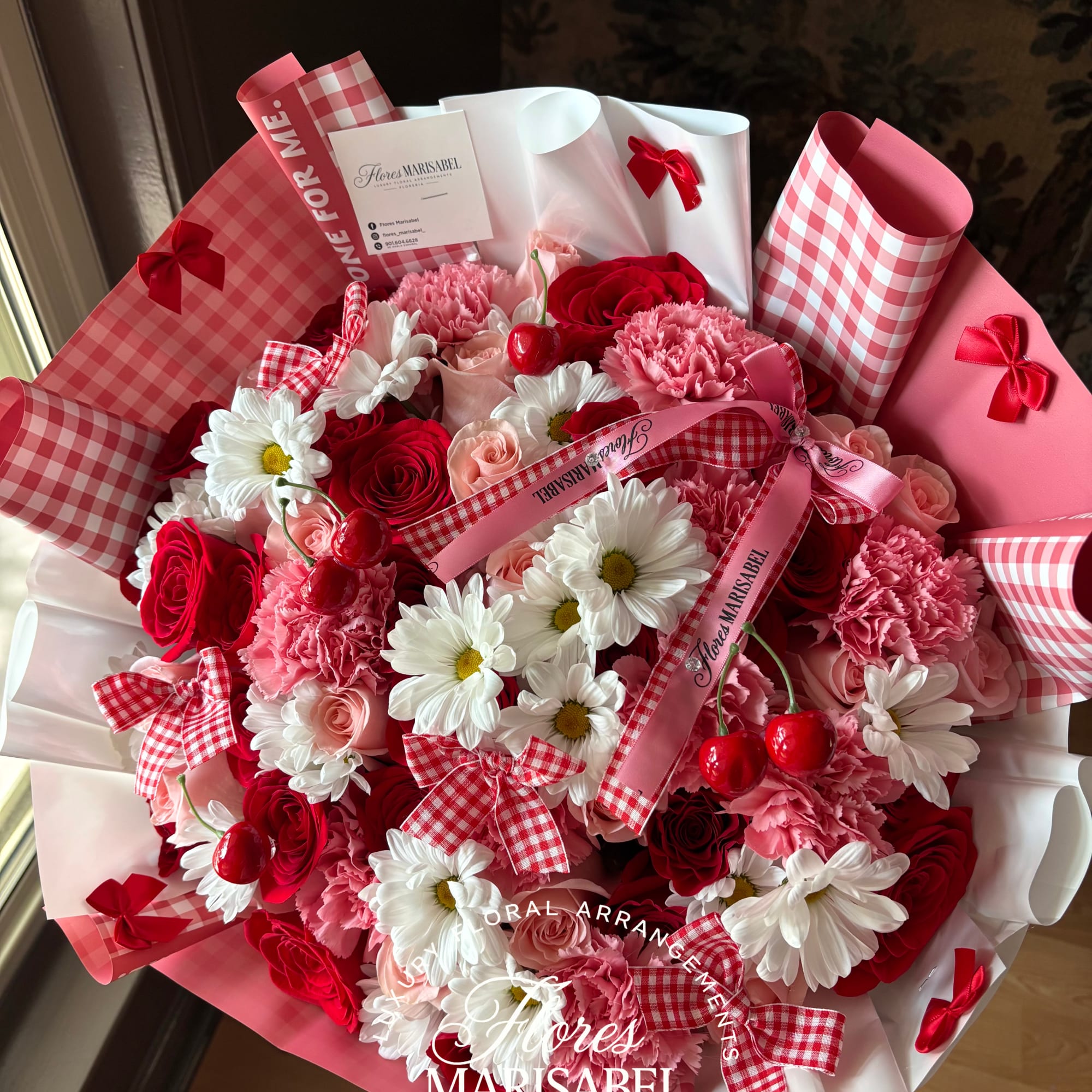 Pink and red bouquet with roses, carnations, and daisies wrapped in gingham paper