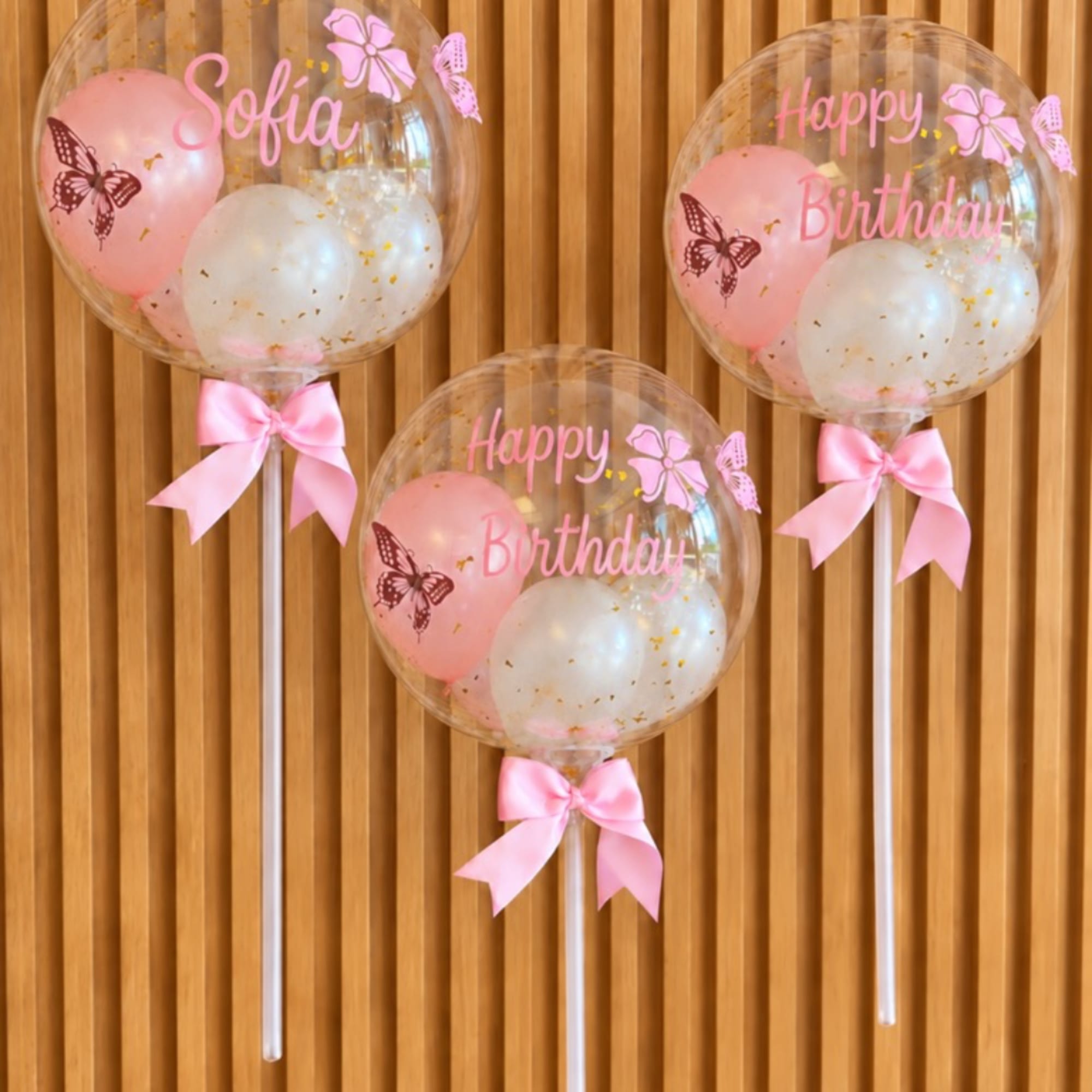 Three clear birthday balloons with pink bows and pastel balloons inside