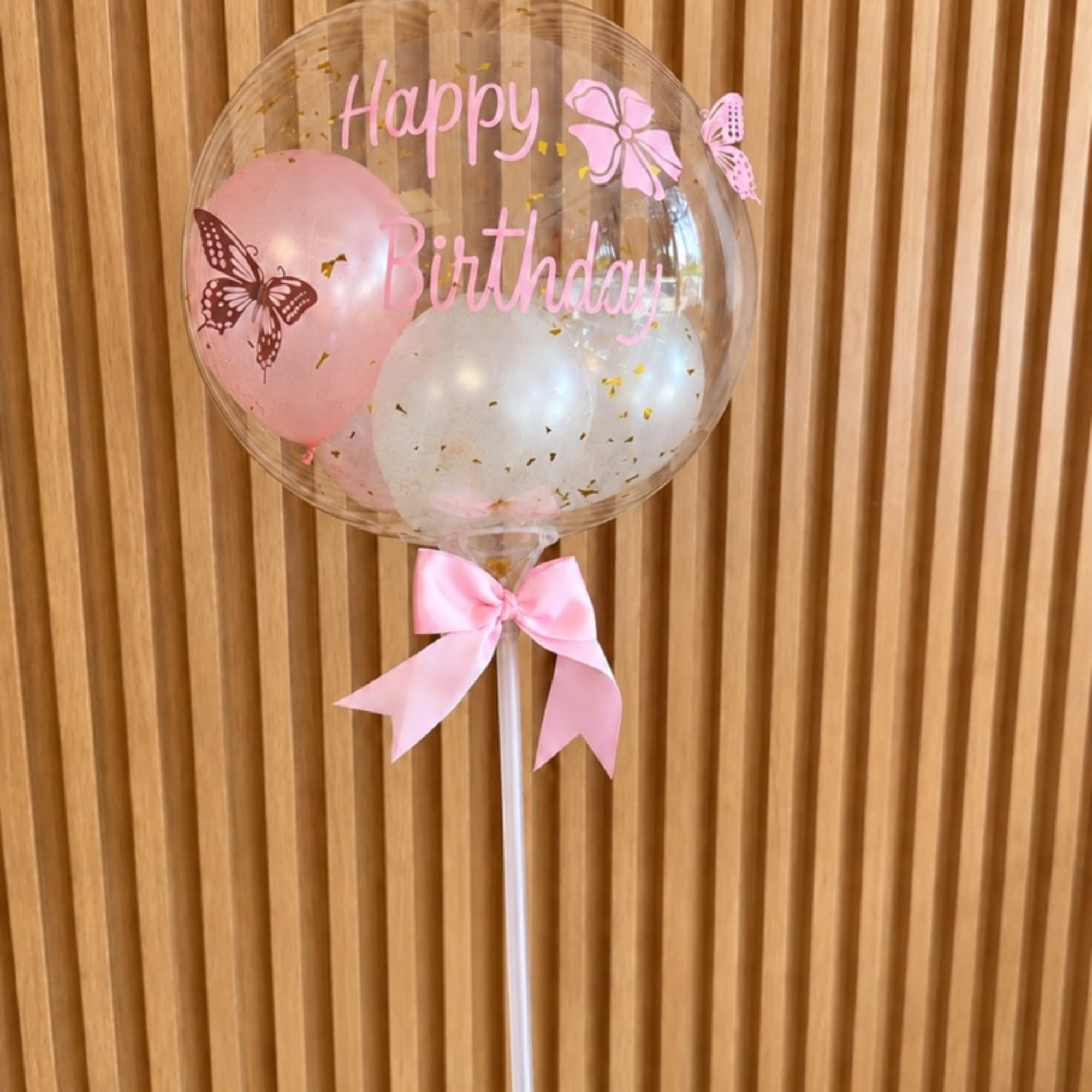 Clear birthday balloon with pink balloons and a ribbon bow