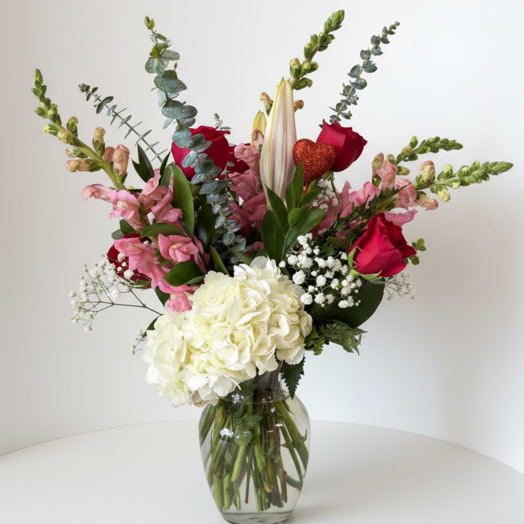 Mixed bouquet with red roses, white hydrangea, pink blooms, and a glass vase