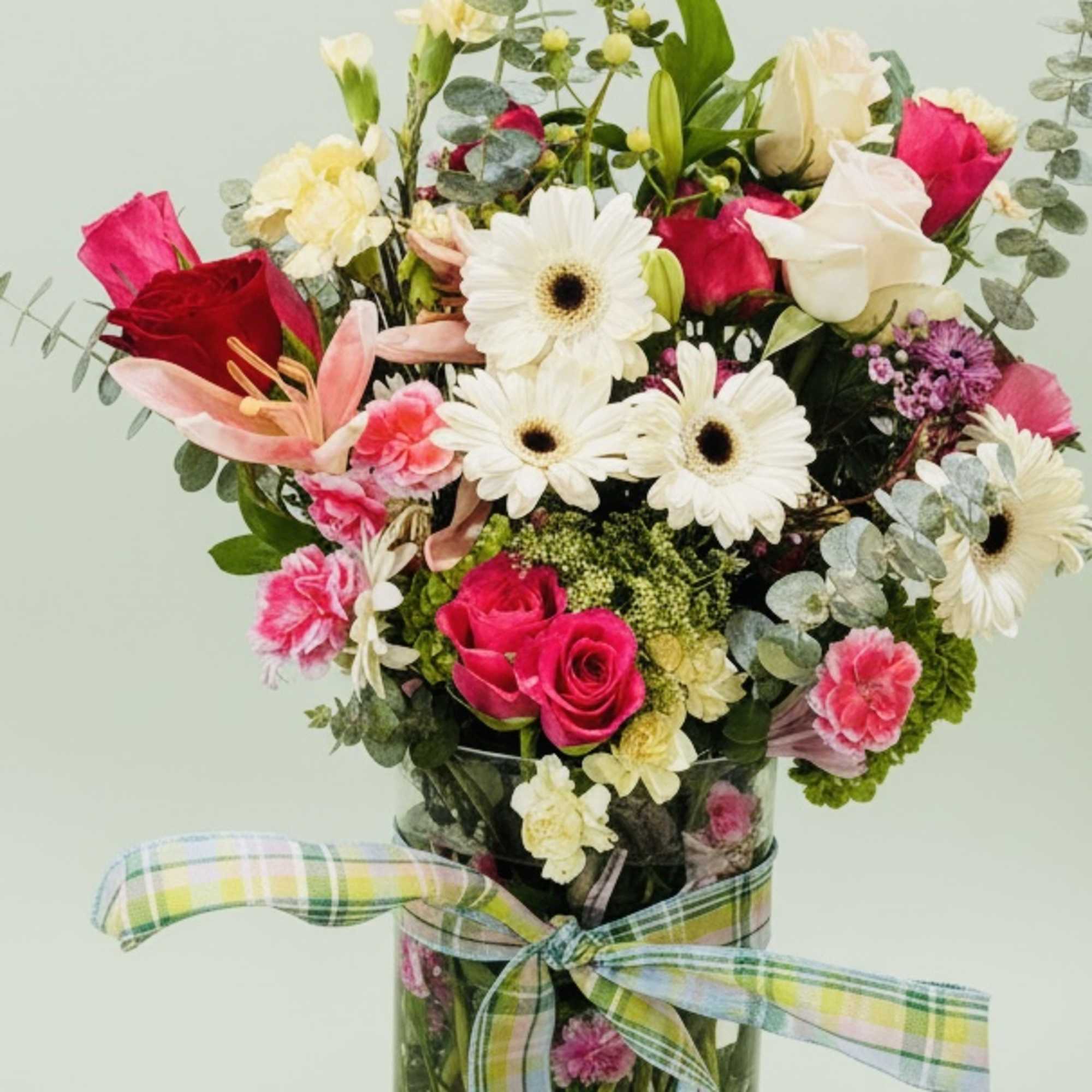 Mixed bouquet of pink and white flowers in a glass vase with a plaid ribbon