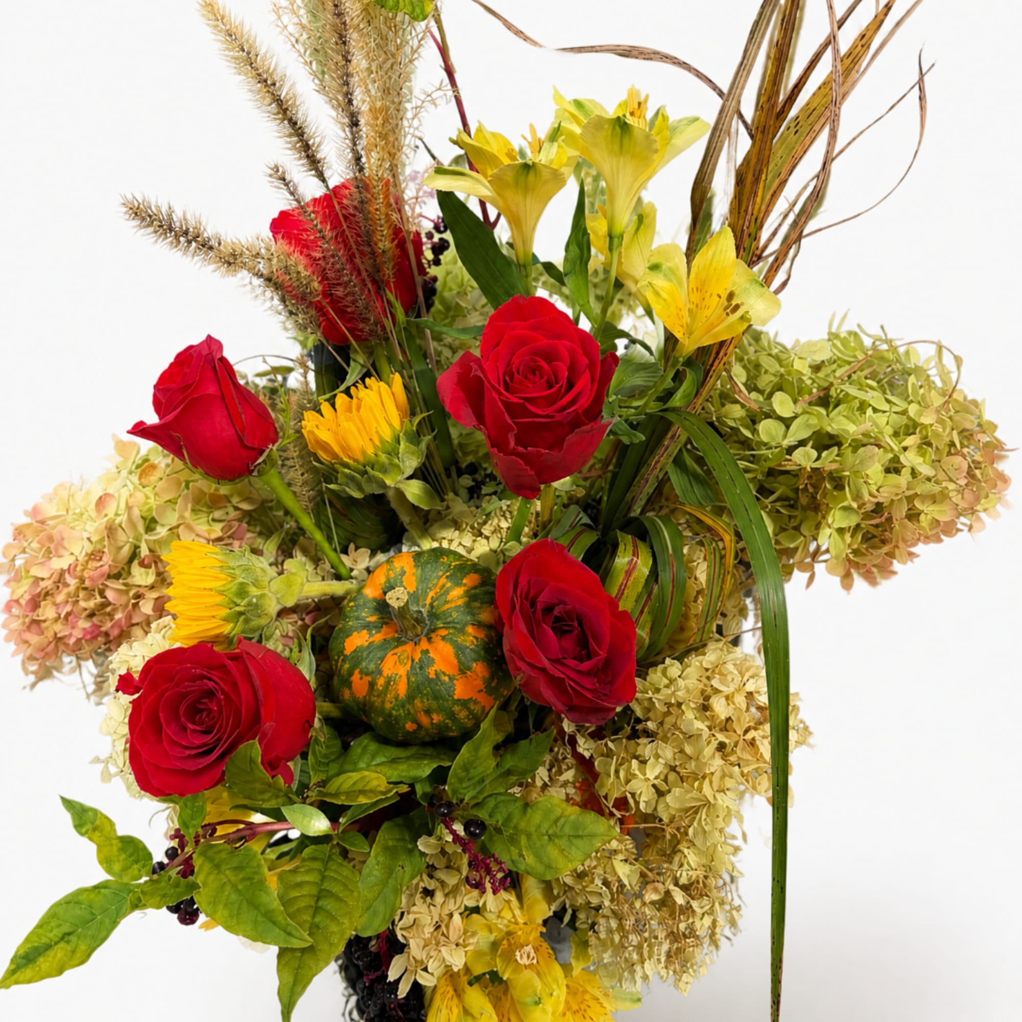 Red roses and yellow lilies arranged with dried grasses and a small pumpkin