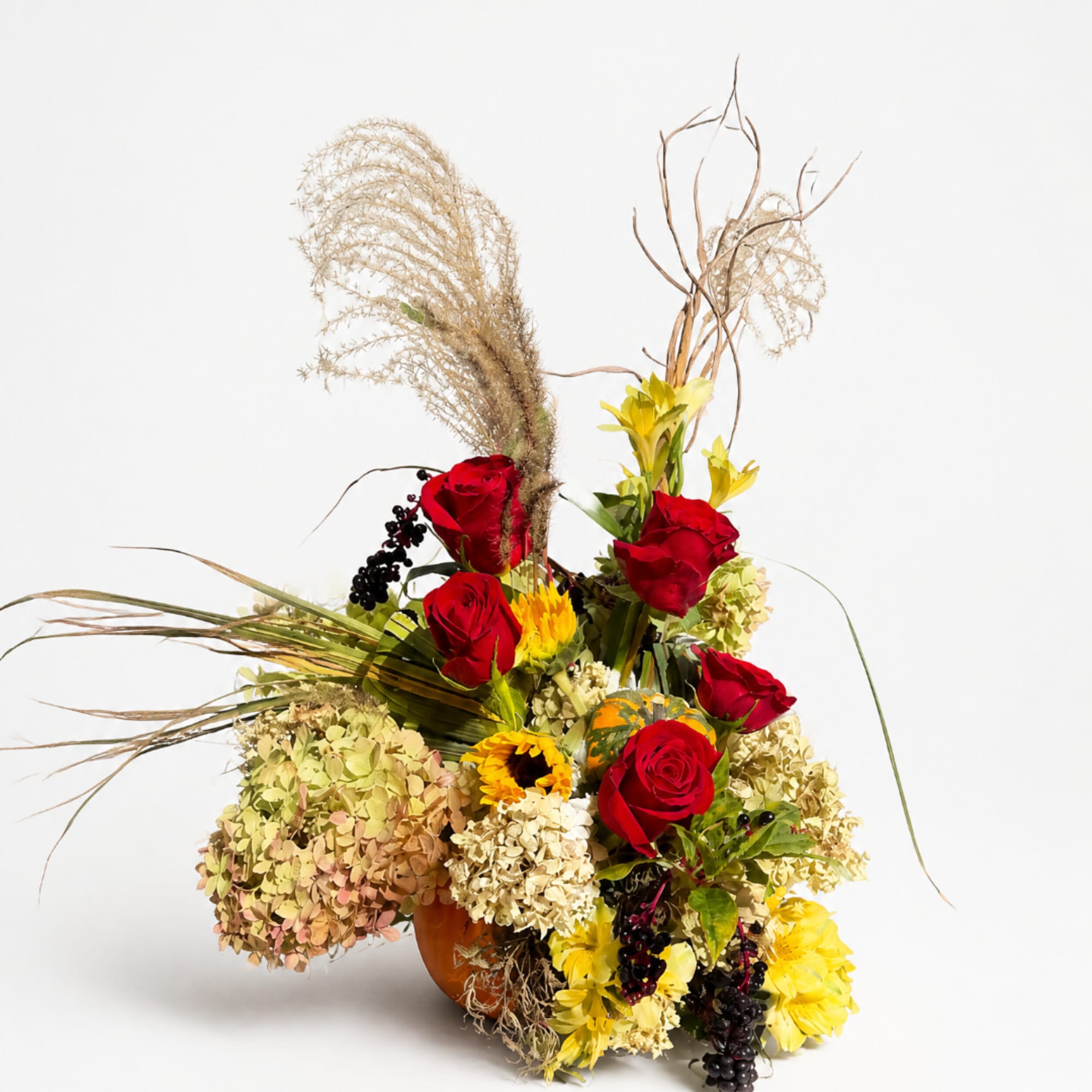 Autumn floral arrangement with red roses, yellow blooms, and dried grasses in a vase