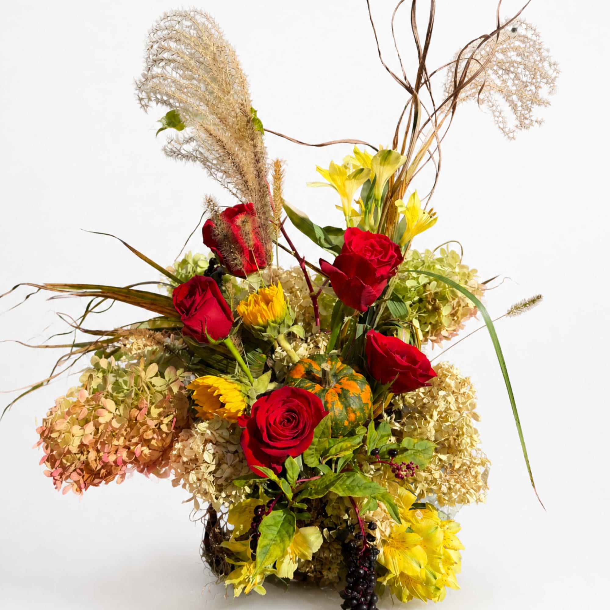 Tall floral arrangement with red roses, yellow blooms, and dried grasses