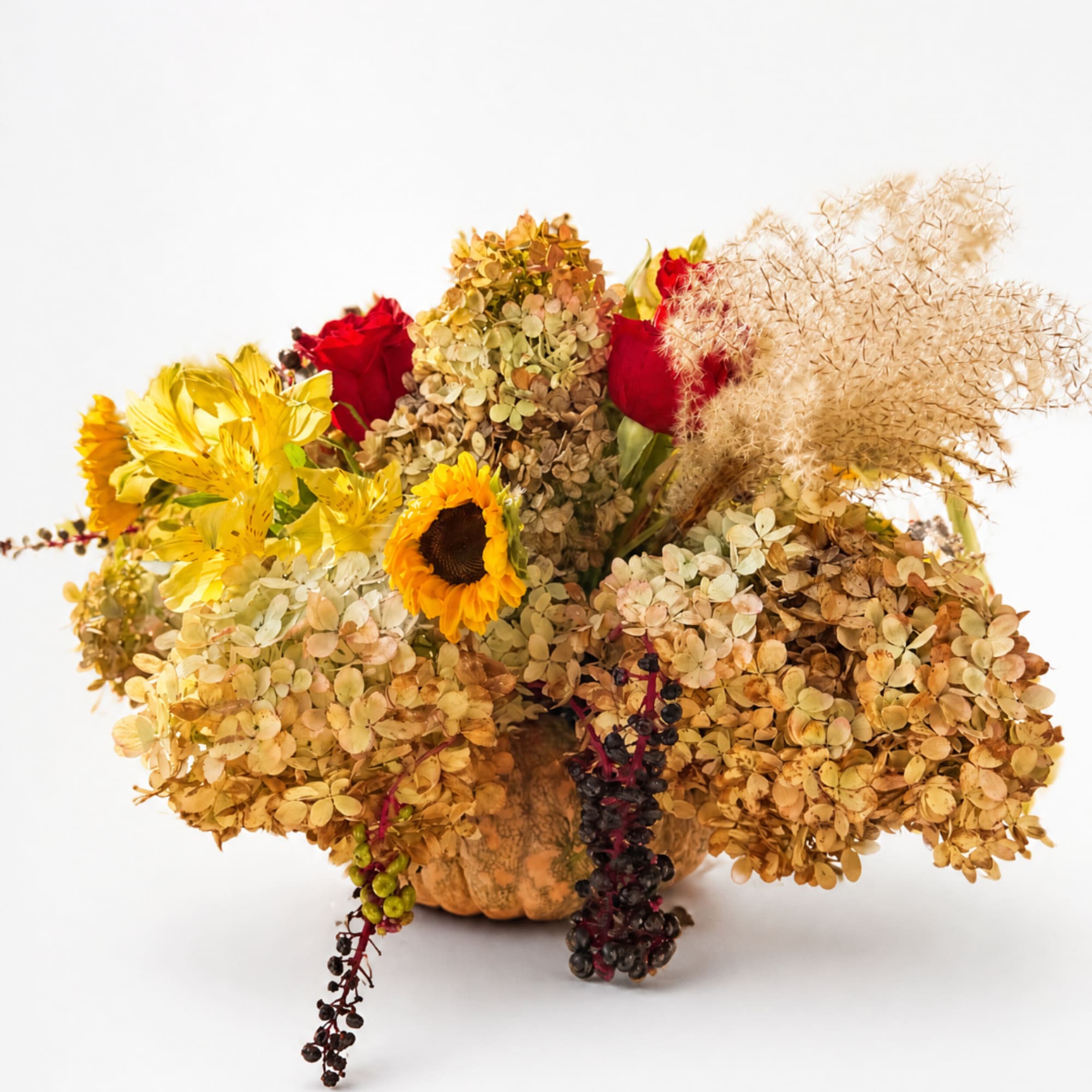 Autumn floral arrangement in a pumpkin container with sunflowers, red roses, and dried hydrangeas