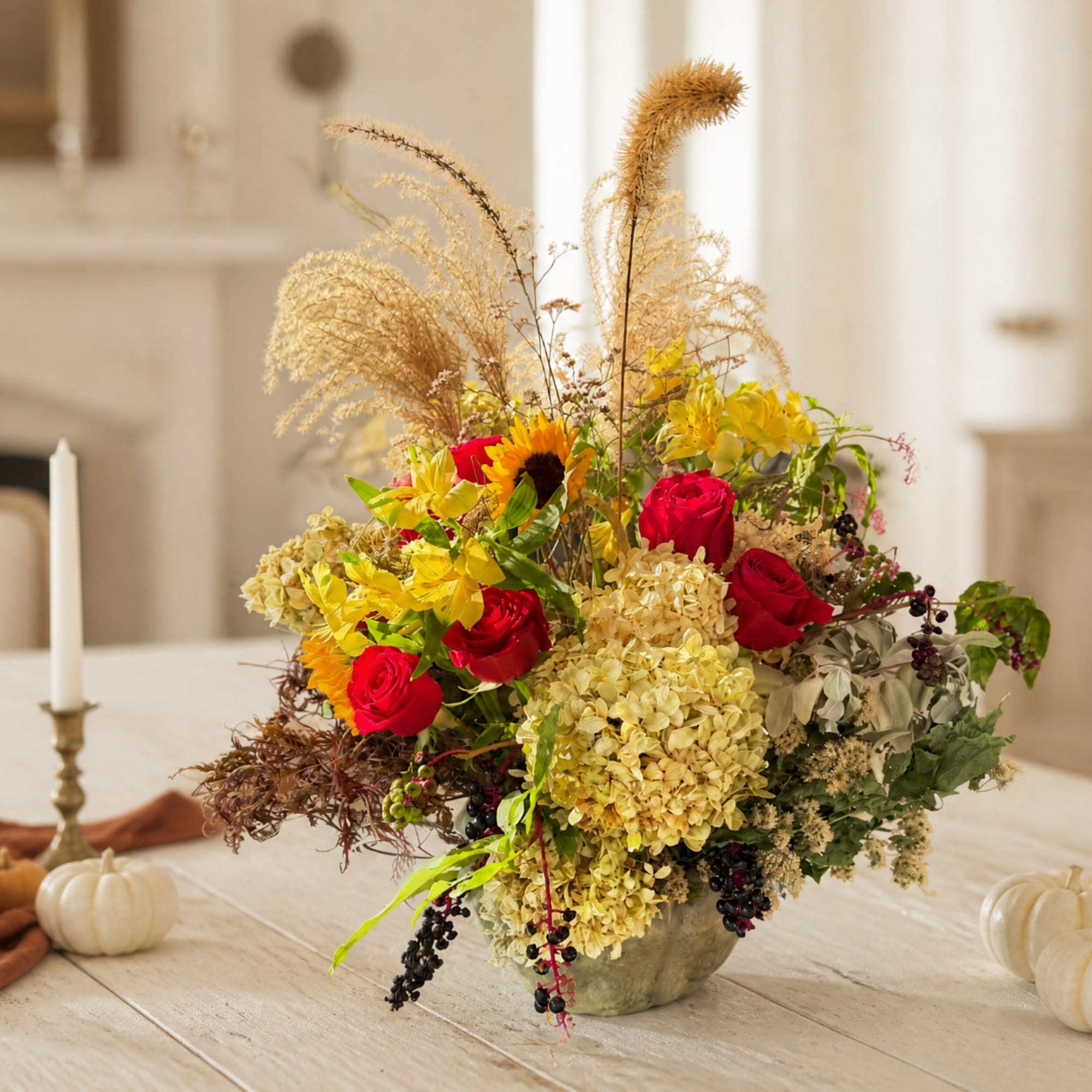 Mixed bouquet with red roses, sunflowers, and dried grasses in a low vase