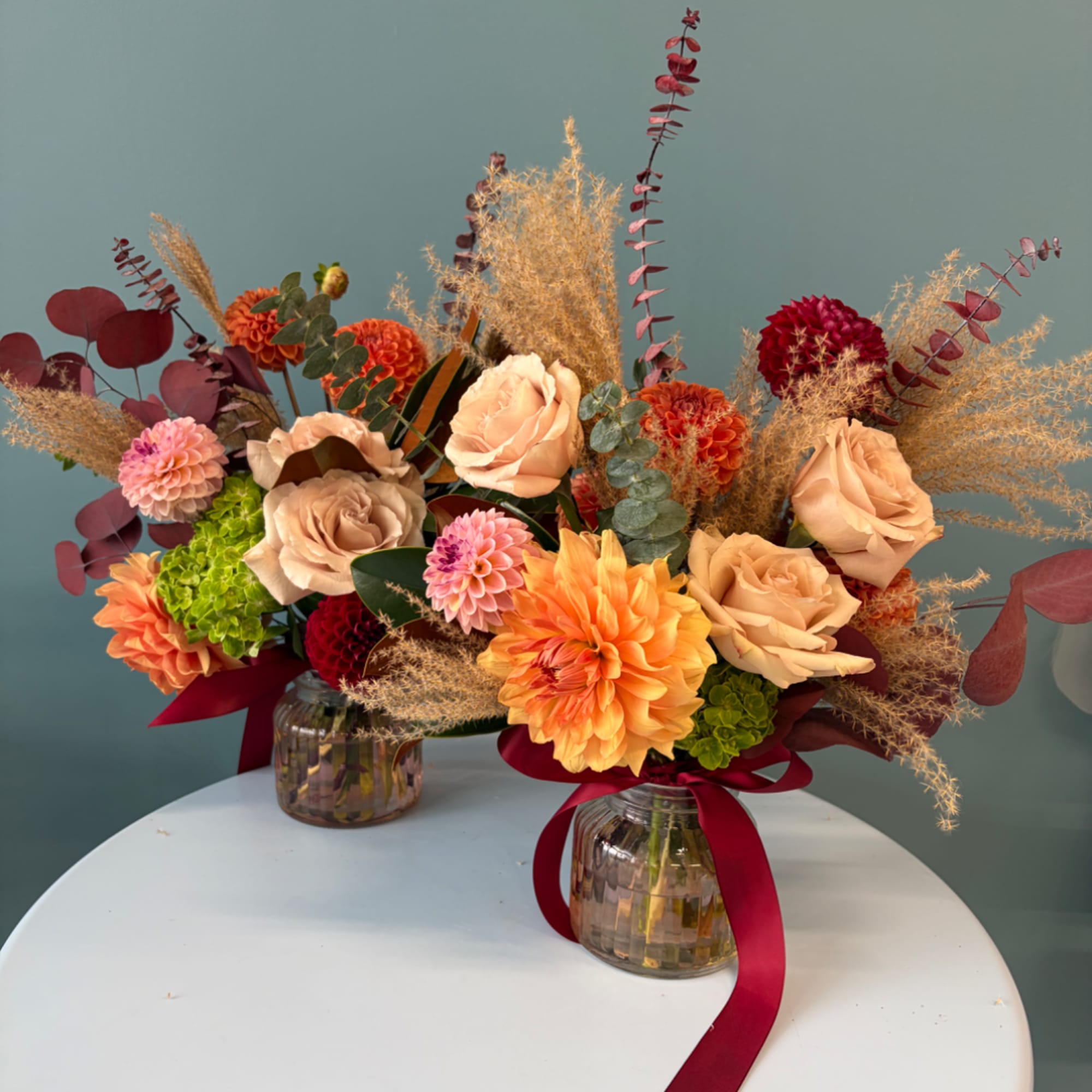 Two floral arrangements in glass jars with peach and orange blooms