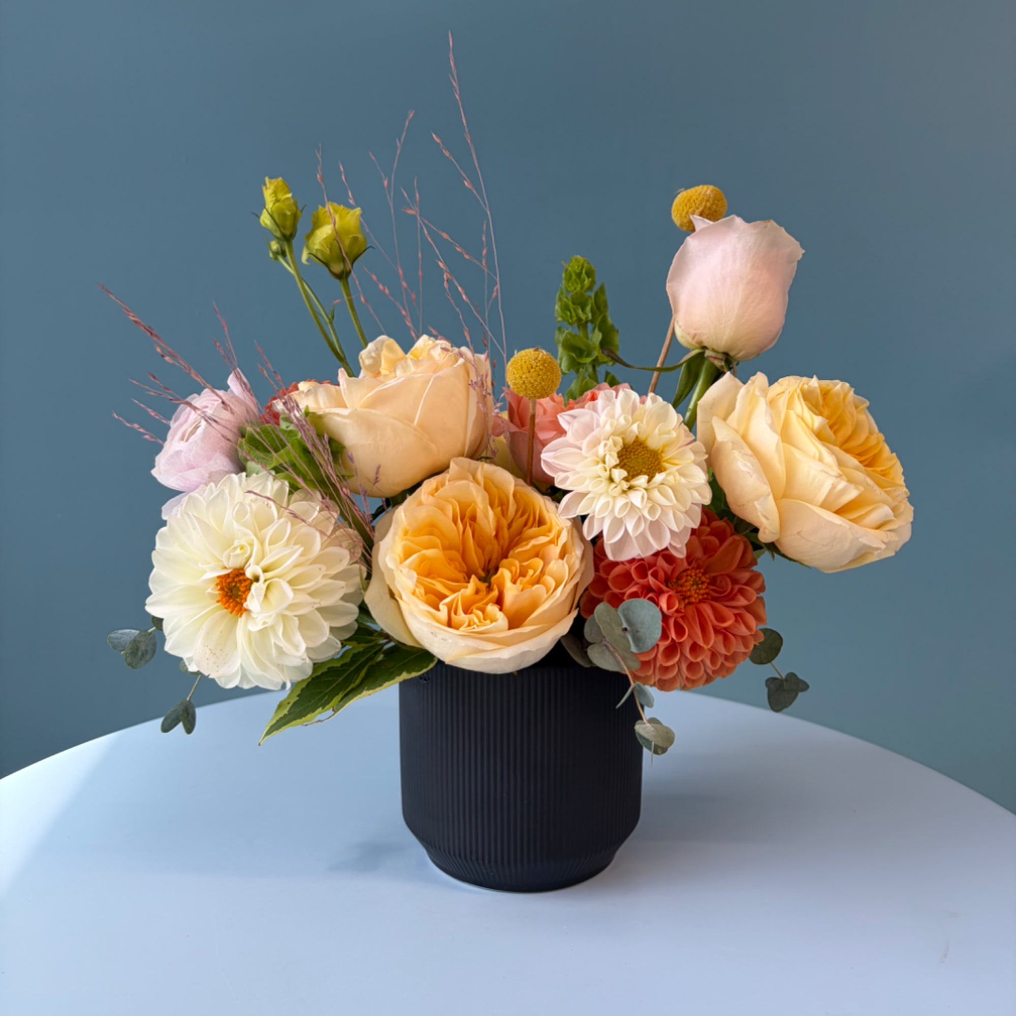 Mixed pastel flowers arranged in a dark vase on a table