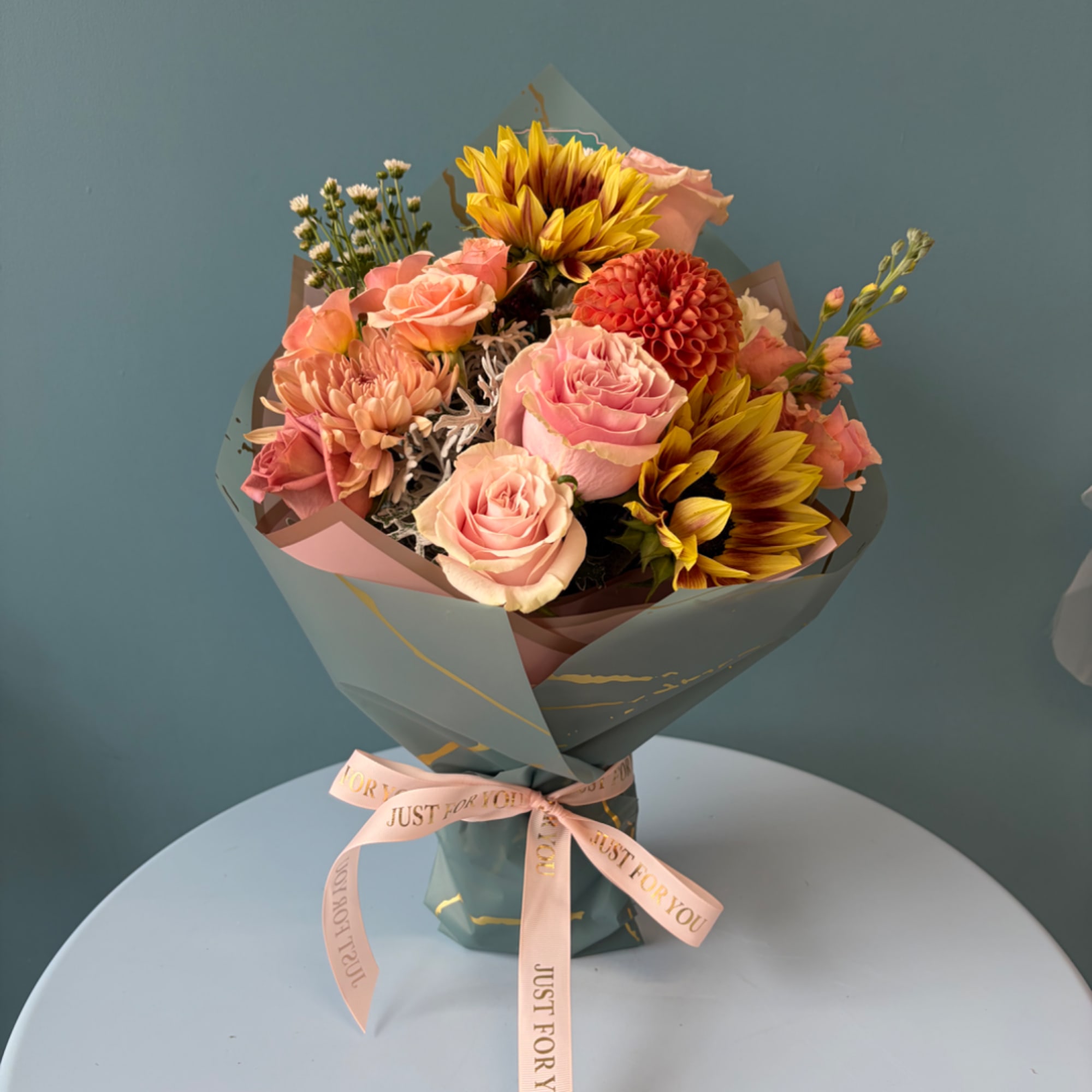 Bouquet of pink roses and sunflowers wrapped in teal paper with a ribbon.
