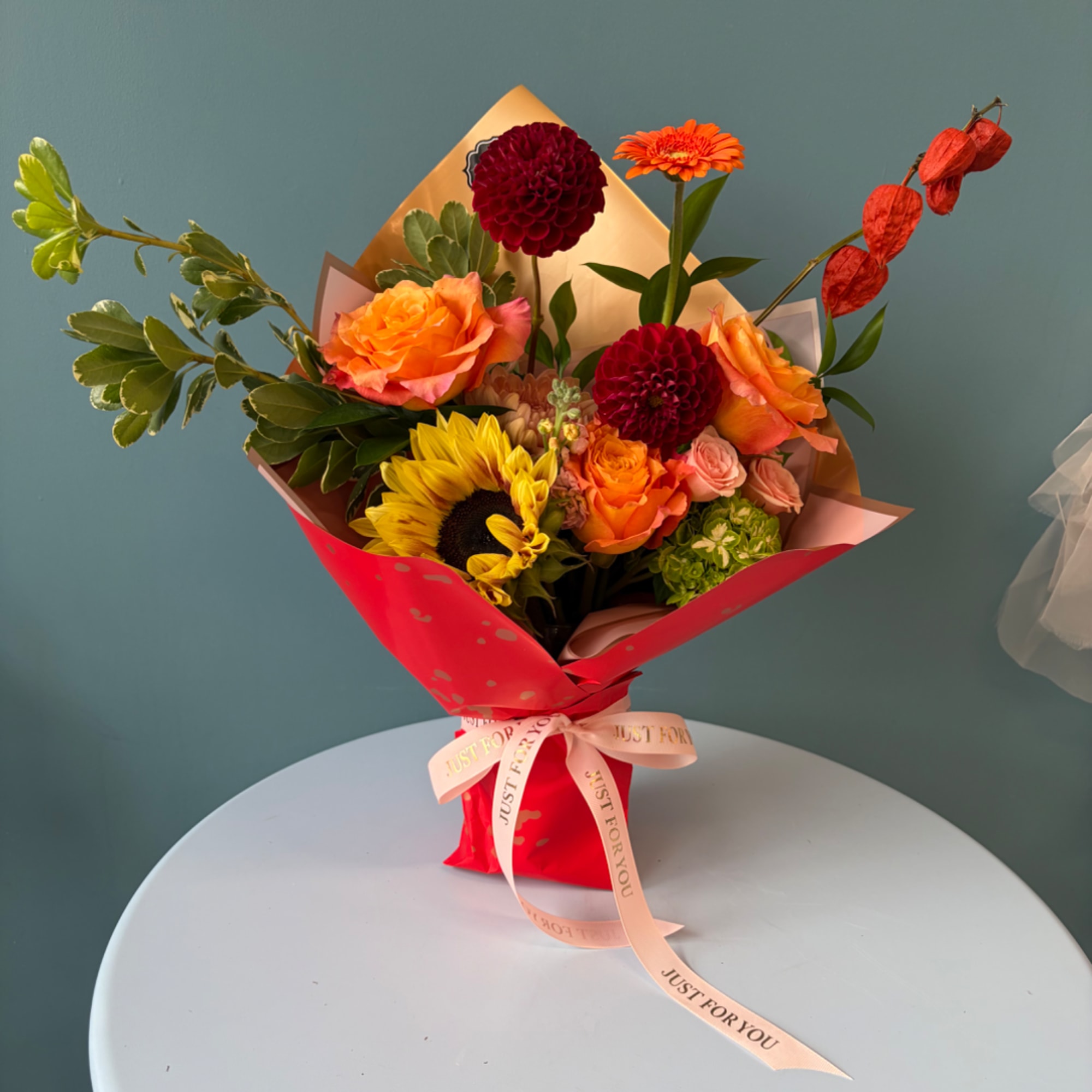 Bouquet of mixed flowers in red wrapping with a ribbon on a table.