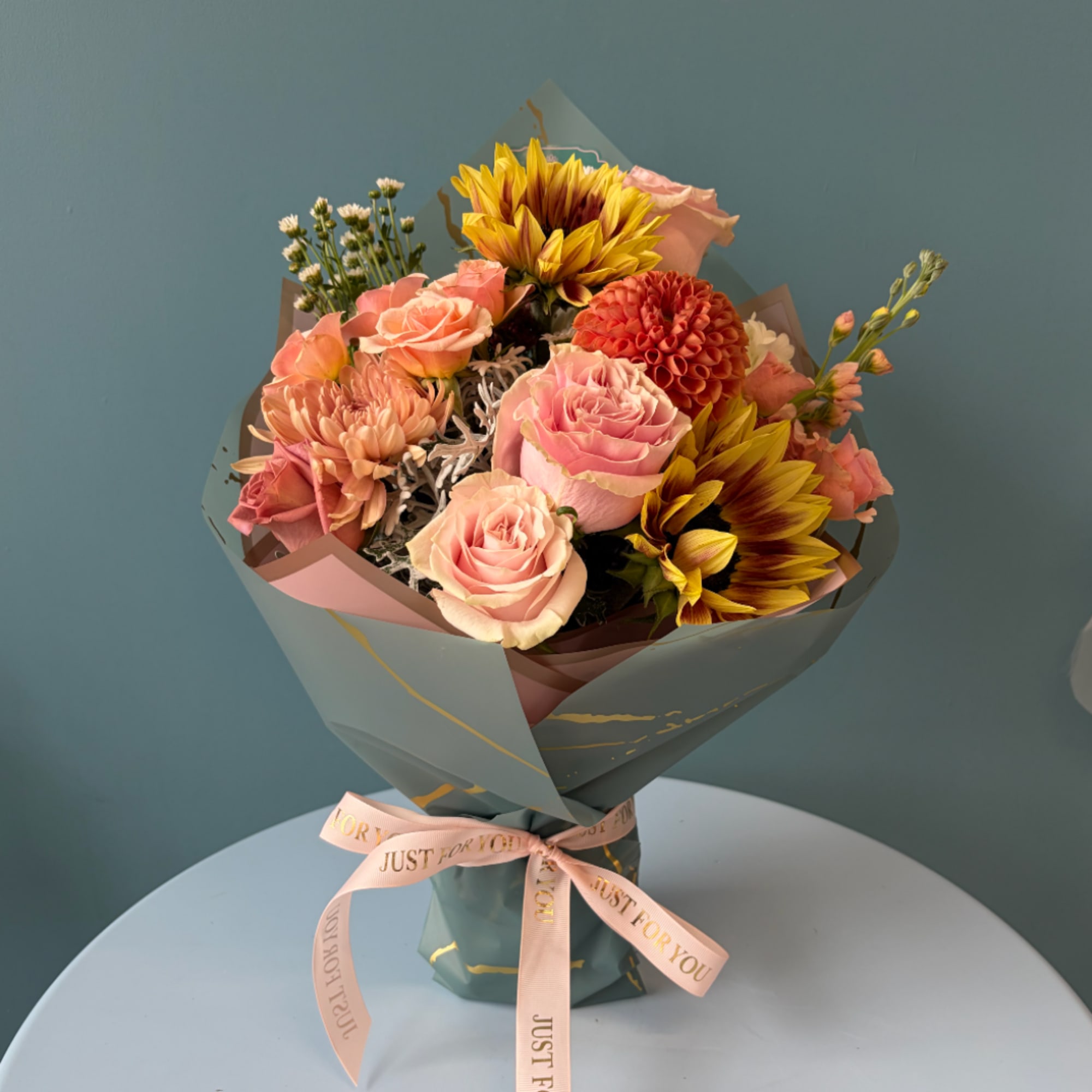 Bouquet of pink roses, dahlias, and sunflowers wrapped in blue paper
