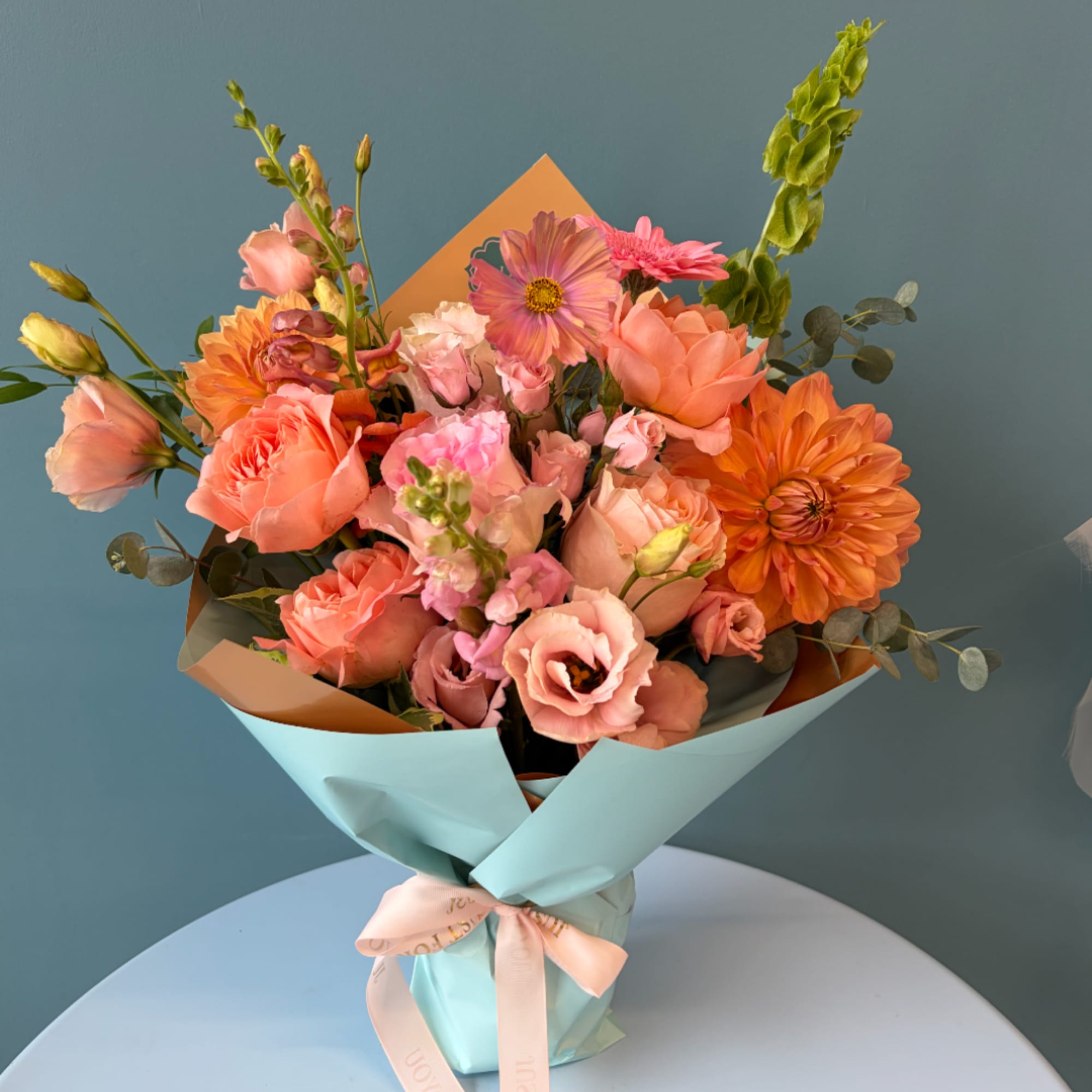 Peach and pink mixed bouquet wrapped in light blue paper with a ribbon