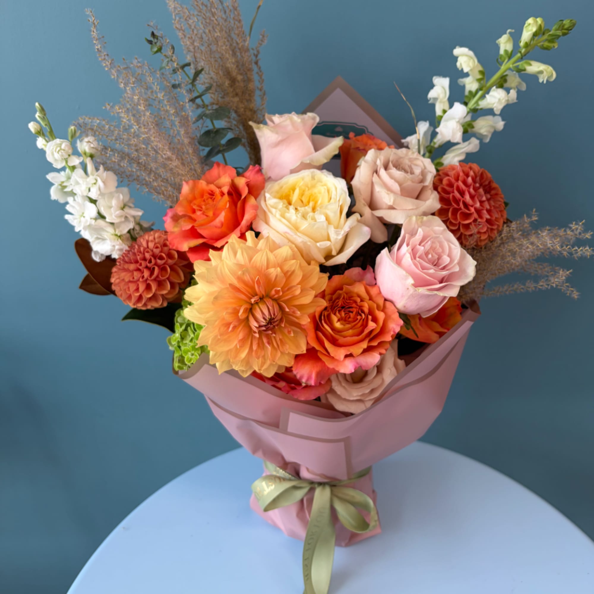 Bouquet of orange, pink, and cream flowers wrapped in pink paper