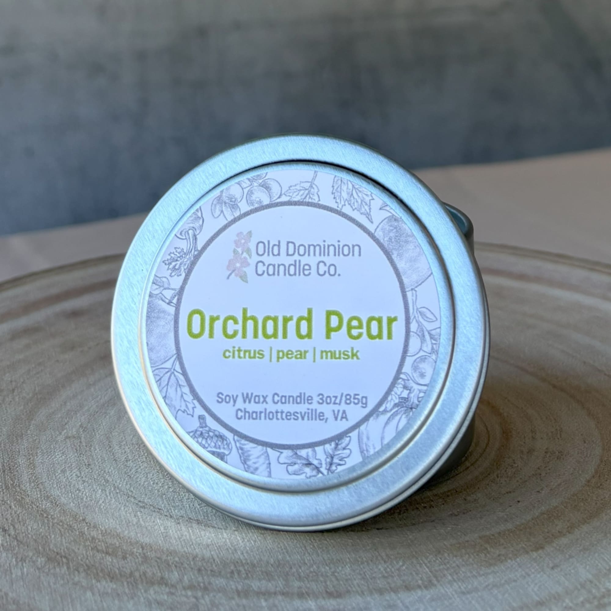 Small tin candle labeled Orchard Pear on a wooden surface