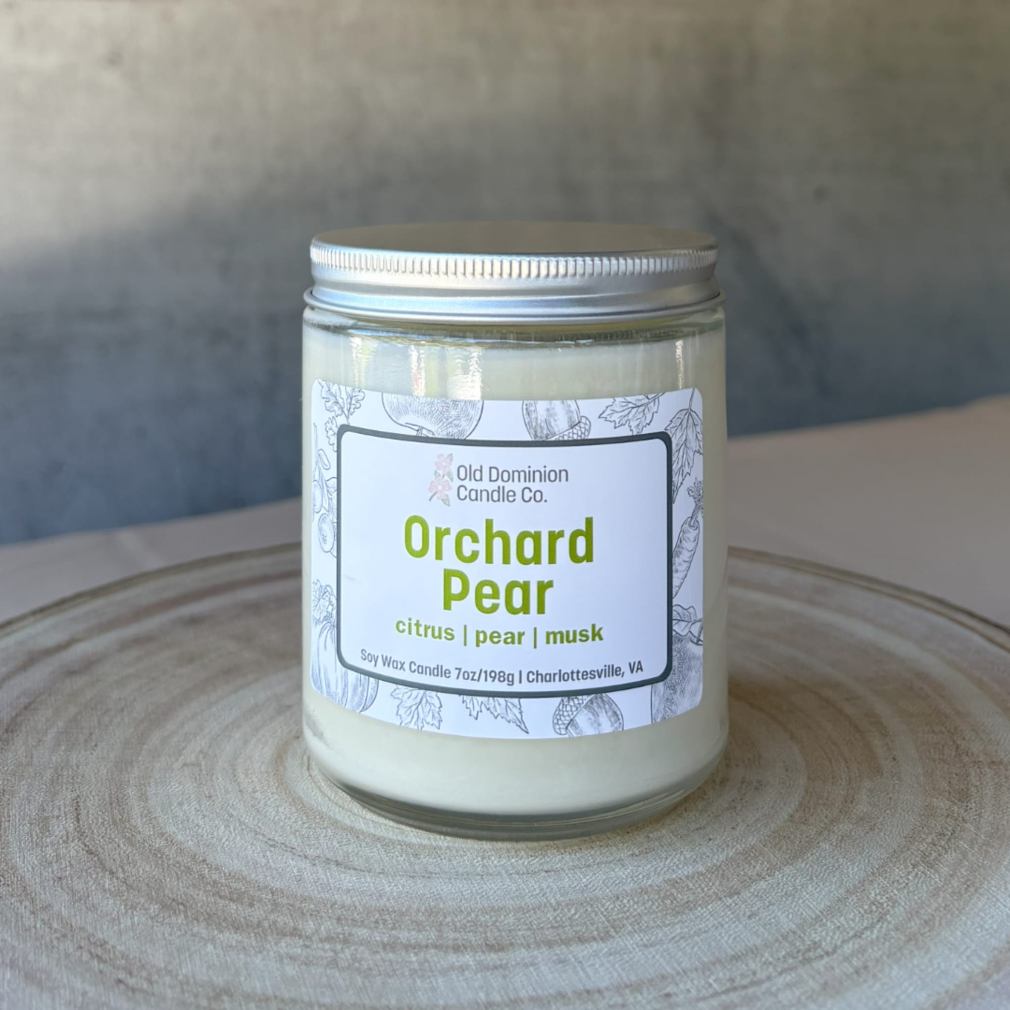 Jar candle labeled Orchard Pear on a wooden surface