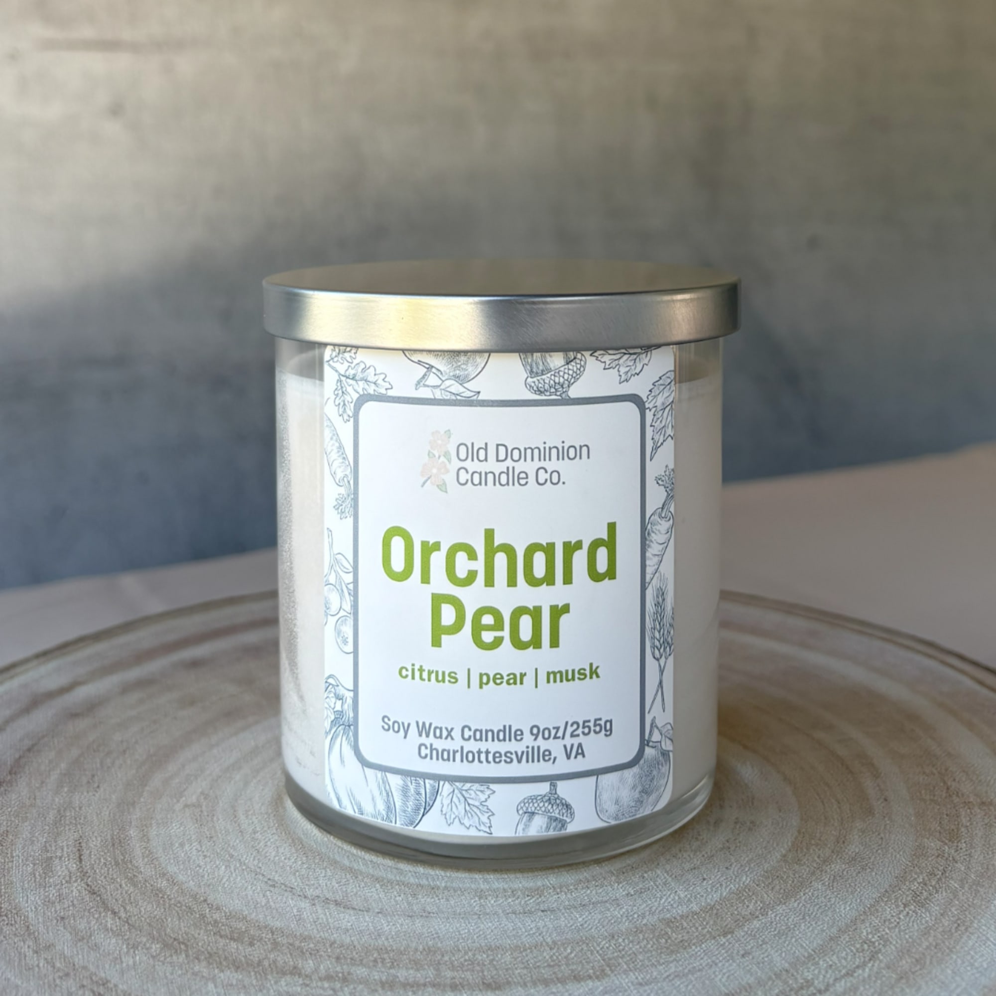 A glass jar candle with a silver lid labeled Orchard Pear