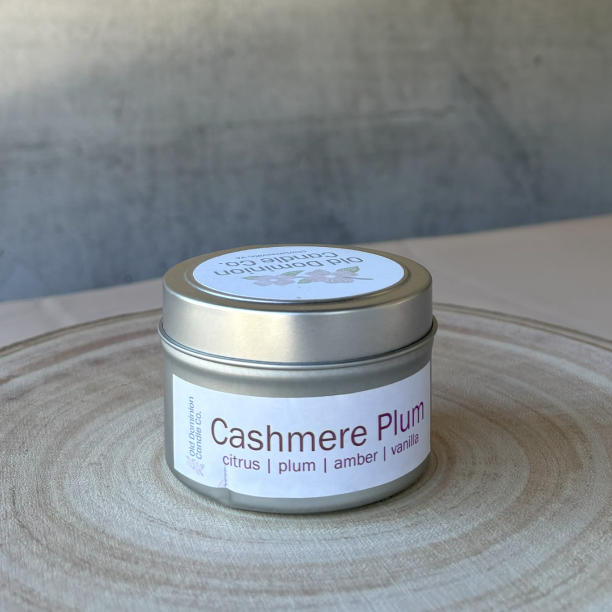 Small metal tin candle labeled Cashmere Plum on a wooden surface