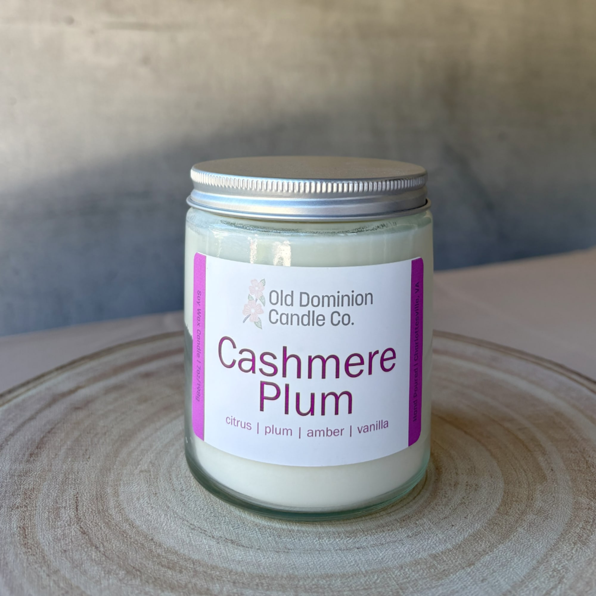 Jar candle labeled Cashmere Plum on a round wooden surface