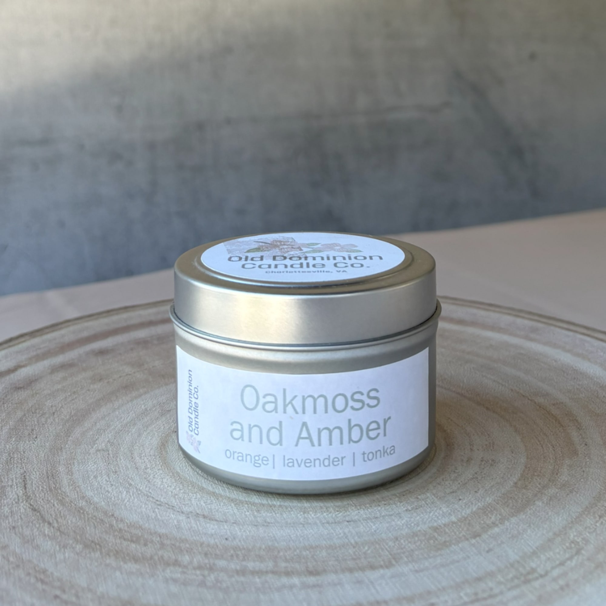 A small tin candle labeled Oakmoss and Amber on a wooden tray