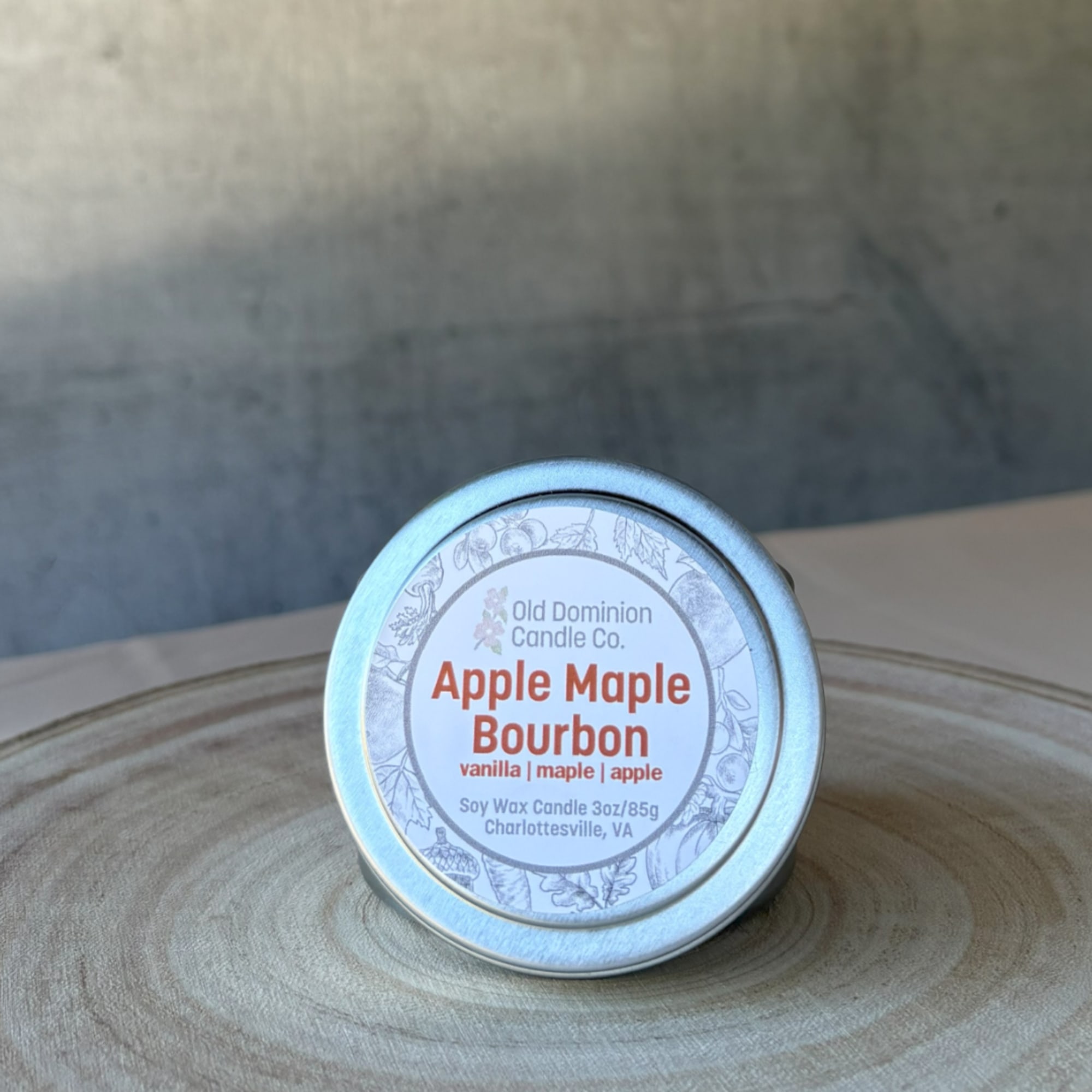 Tin candle labeled Apple Maple Bourbon on a wooden surface