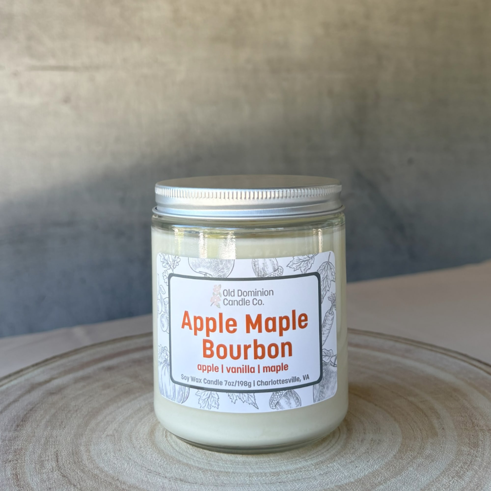 Jar candle labeled Apple Maple Bourbon on a wooden surface