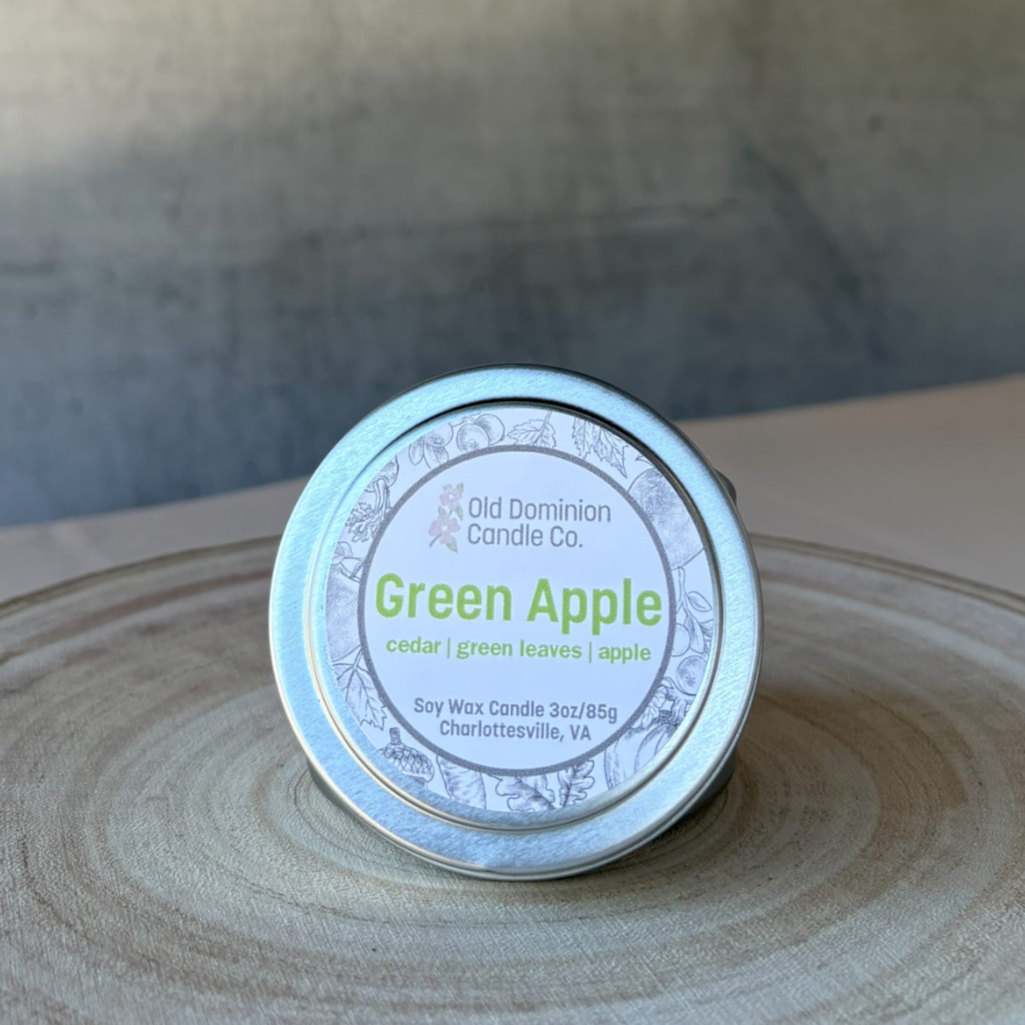 Small tin candle labeled Green Apple on a wooden surface