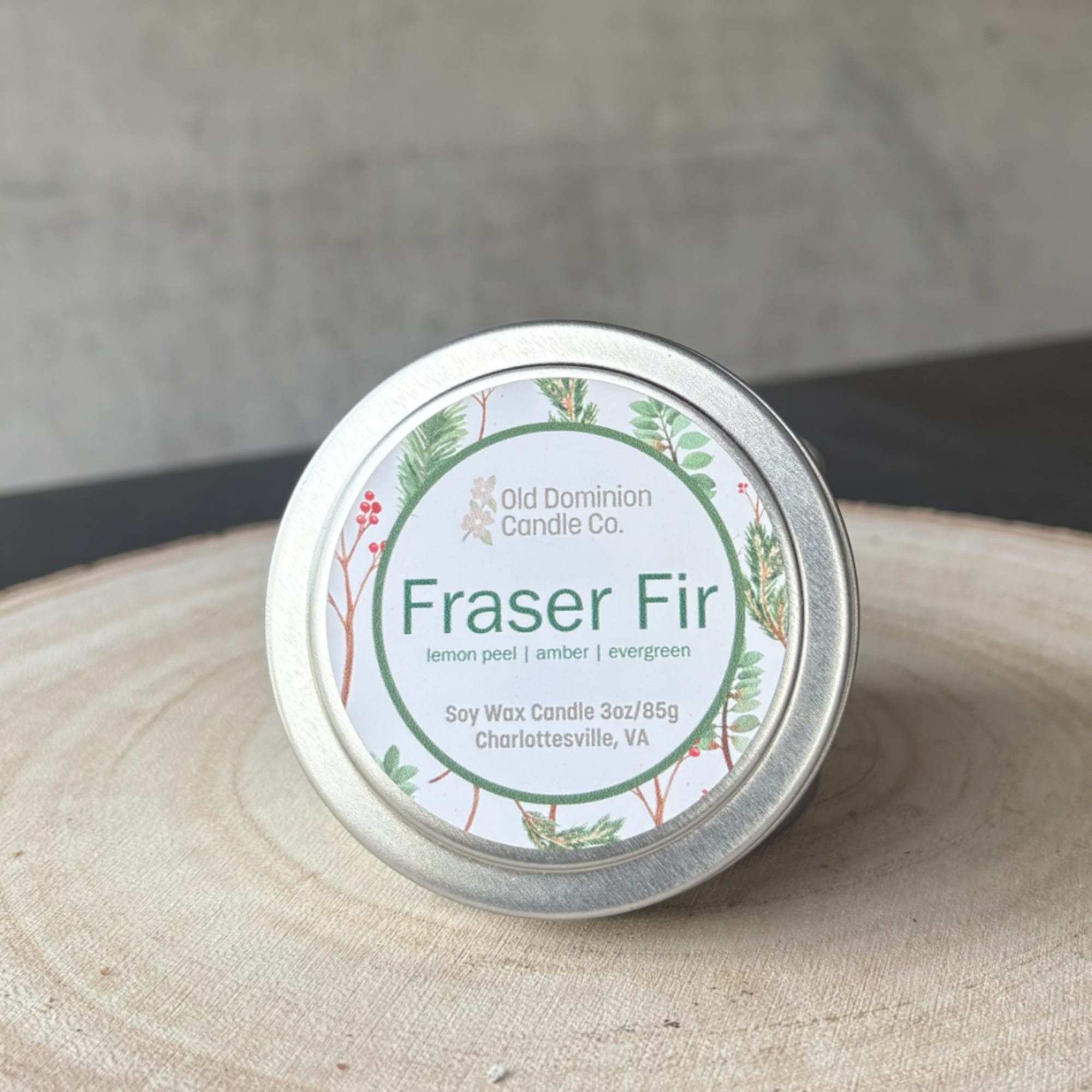 Small tin candle labeled Fraser Fir on a wooden surface