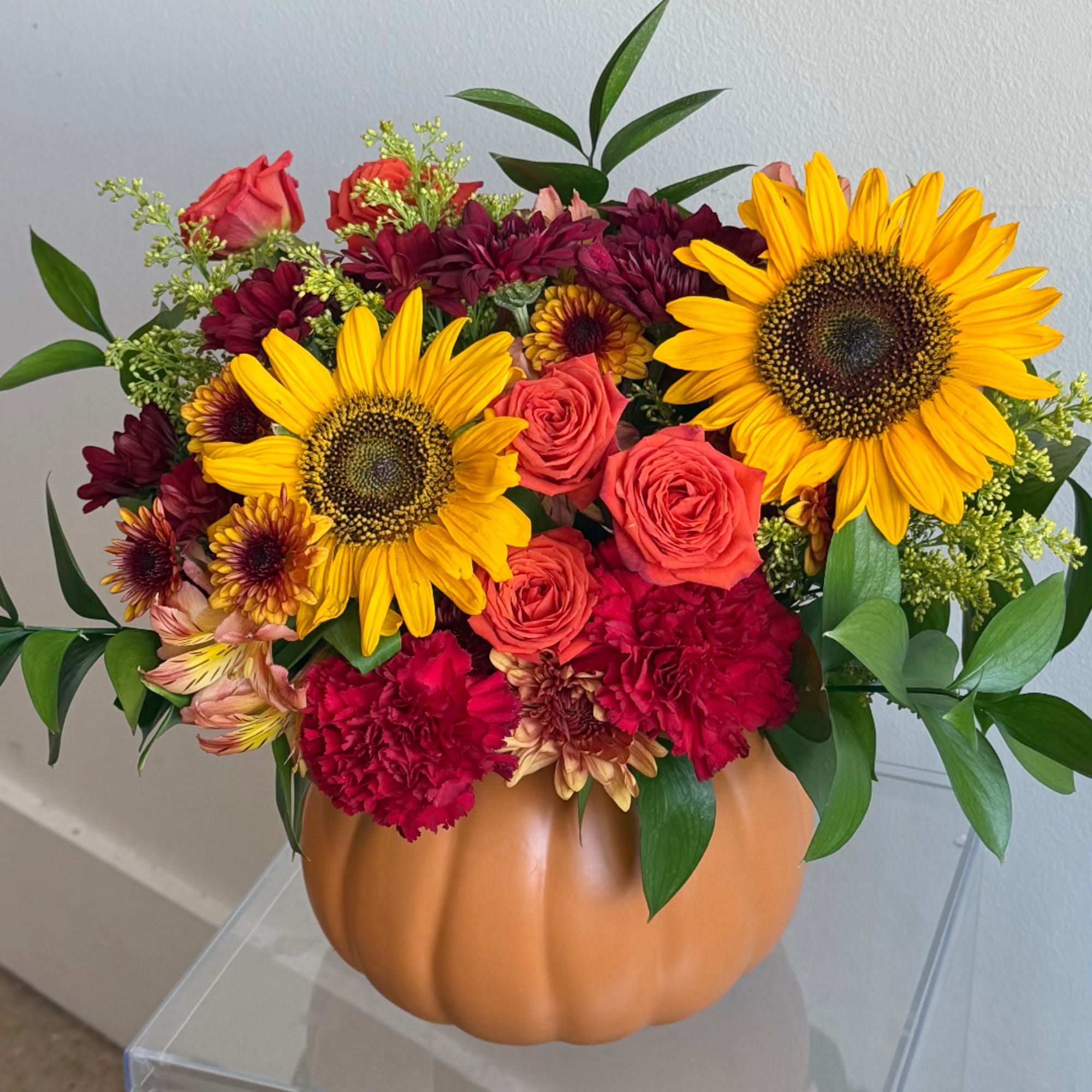 Mixed bouquet of sunflowers, roses, and carnations in a pumpkin vase