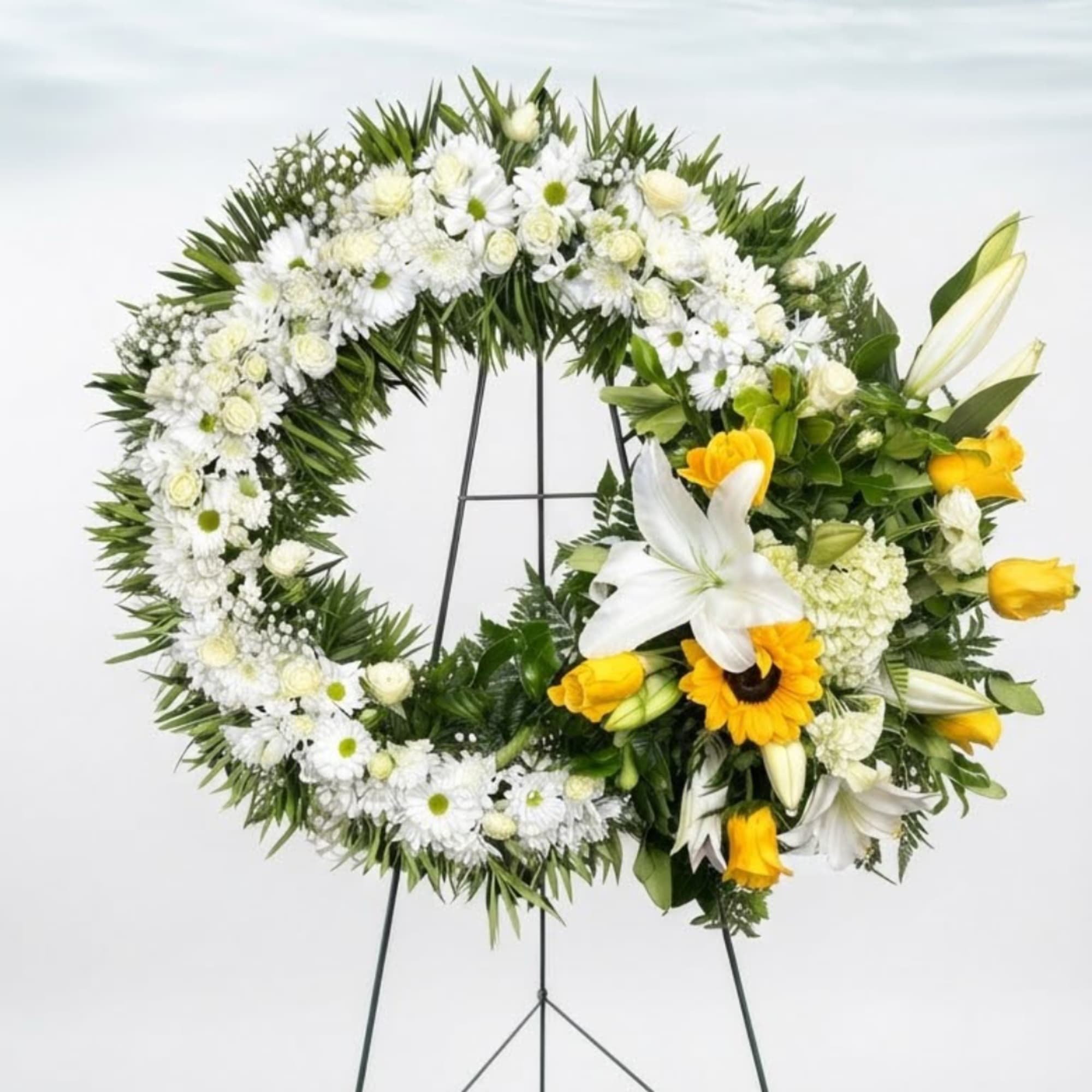 White floral funeral wreath with yellow accents on a stand