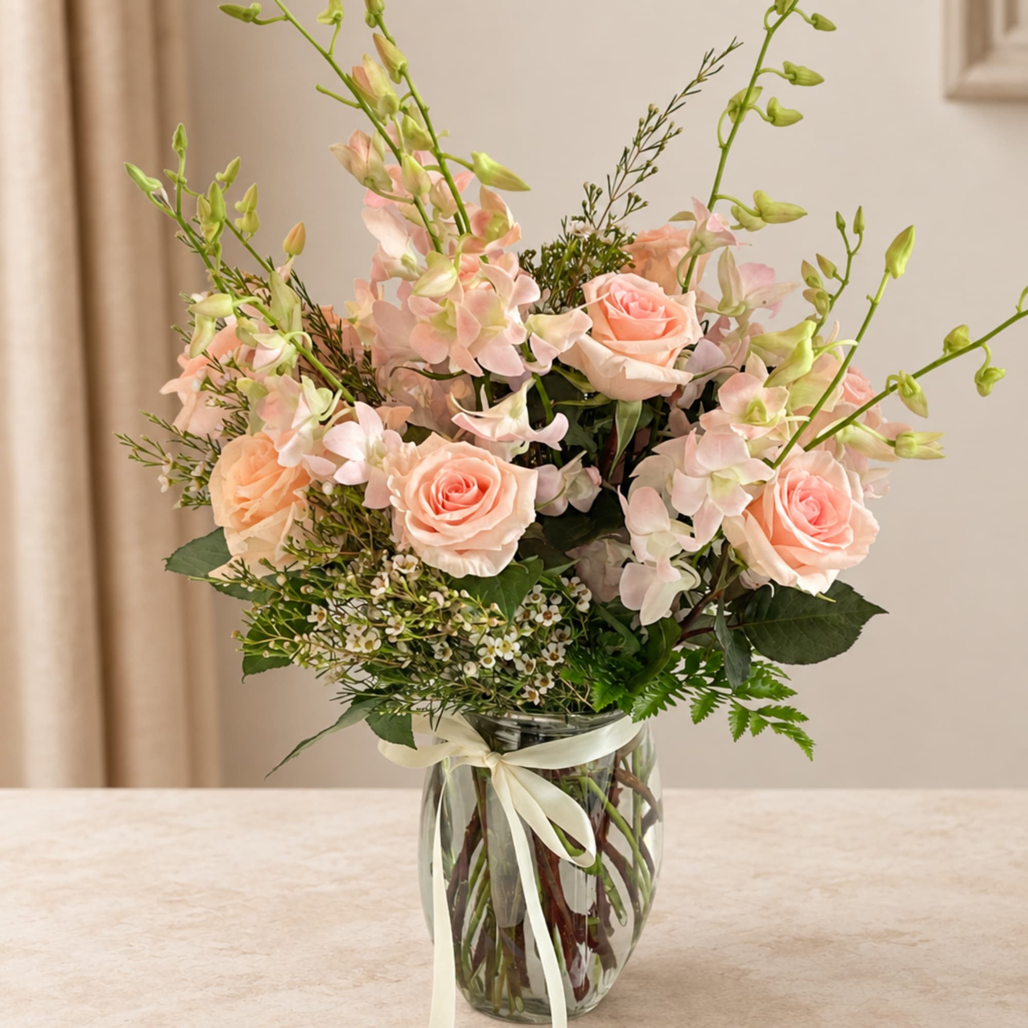 Peach roses and pale pink flowers in a glass vase with a ribbon