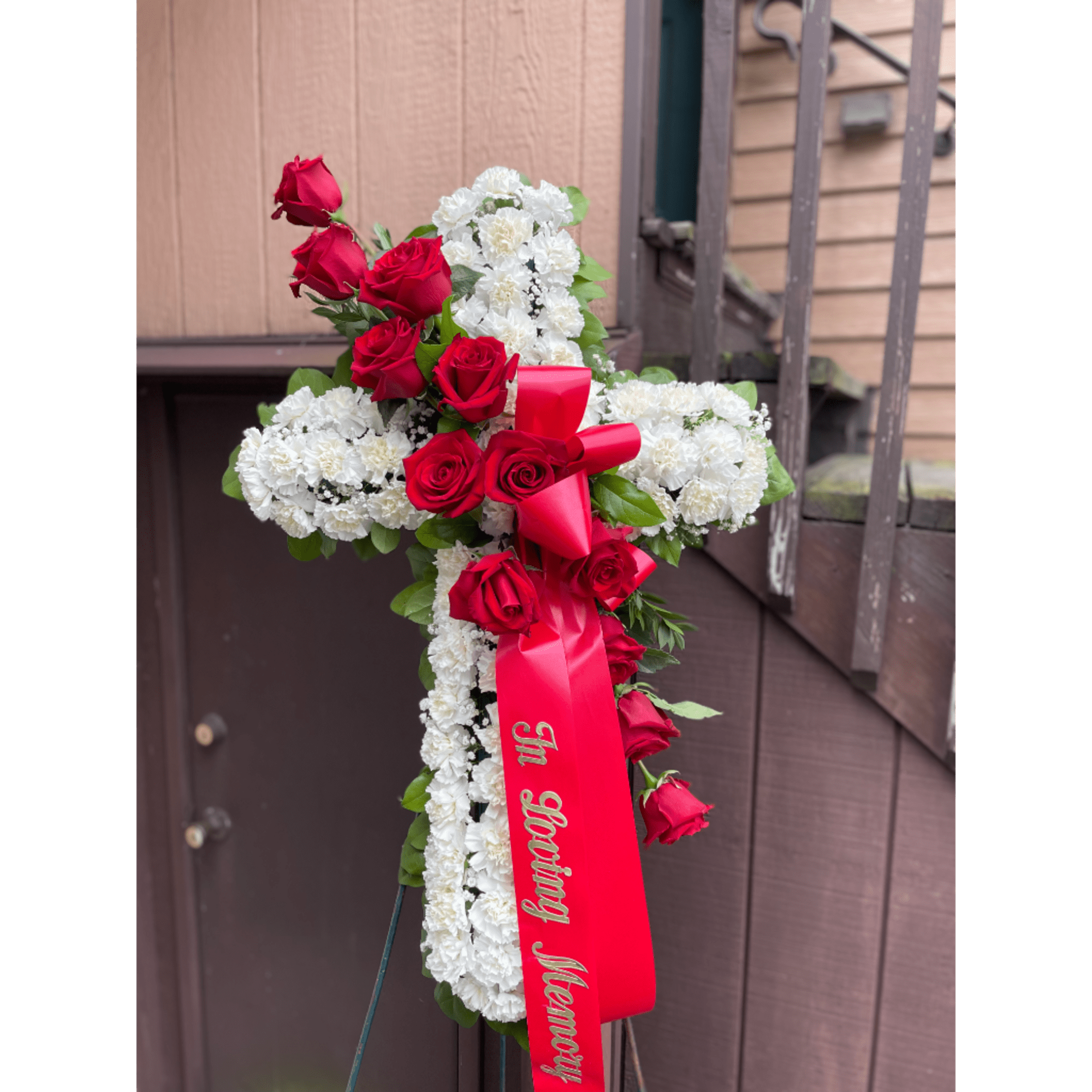 Red roses and white flowers arranged in a cross with a red ribbon