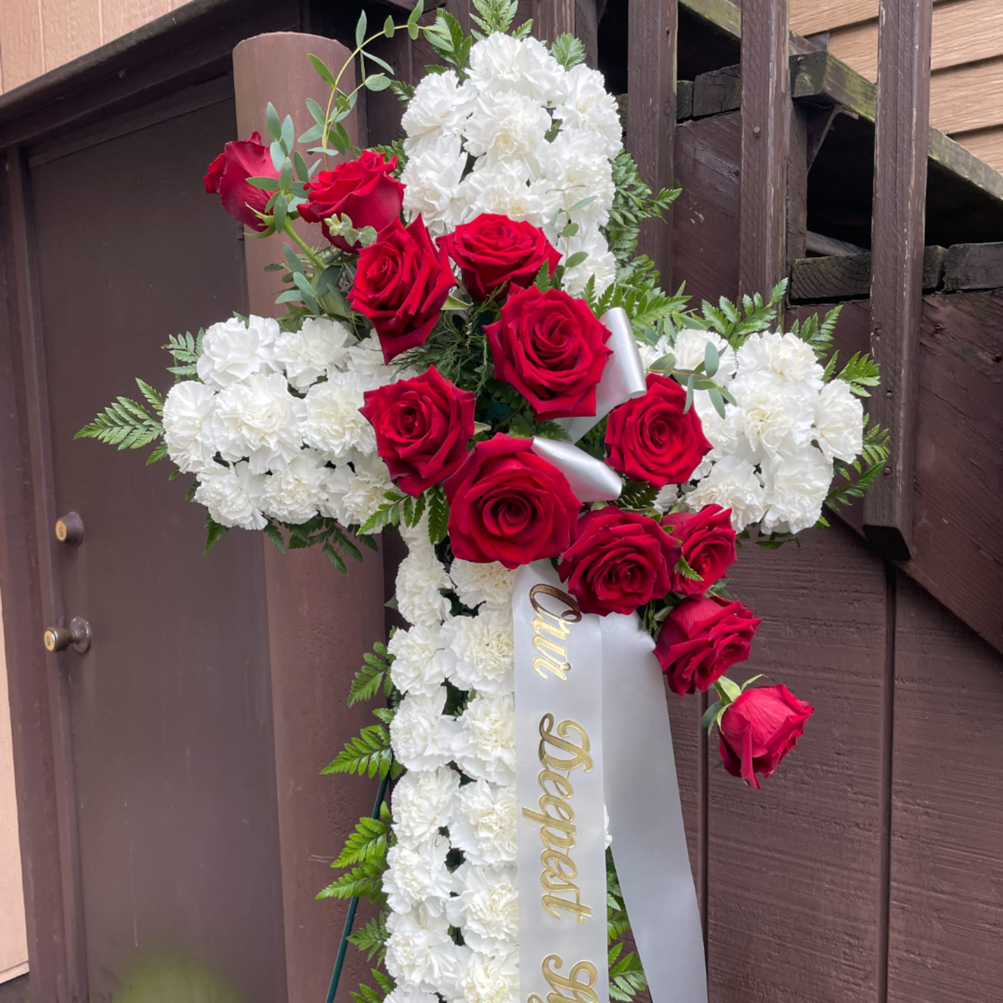 Cross-shaped floral tribute with red roses and white carnations on a stand.